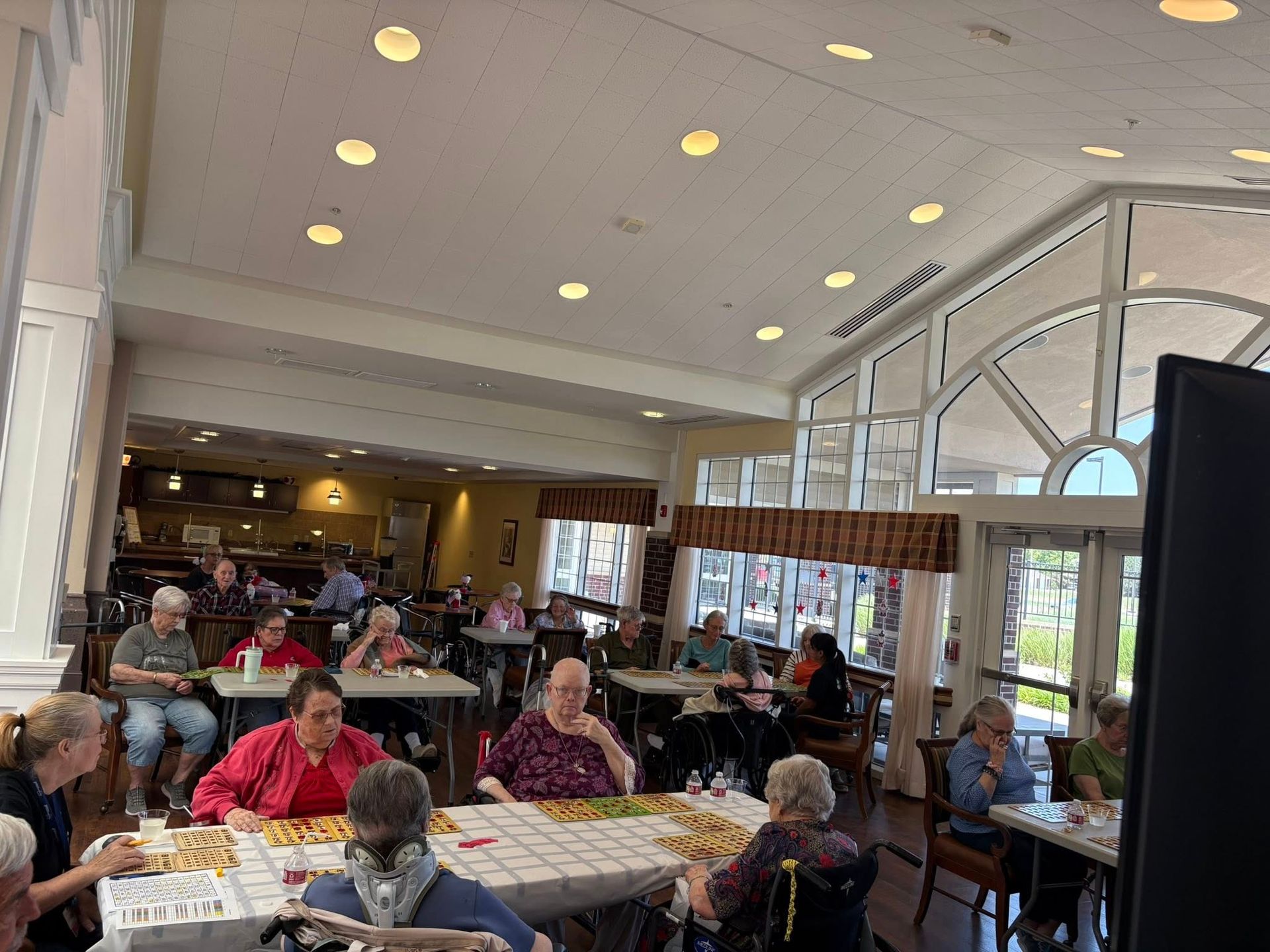 People playing games at tables in a bright room with large windows.