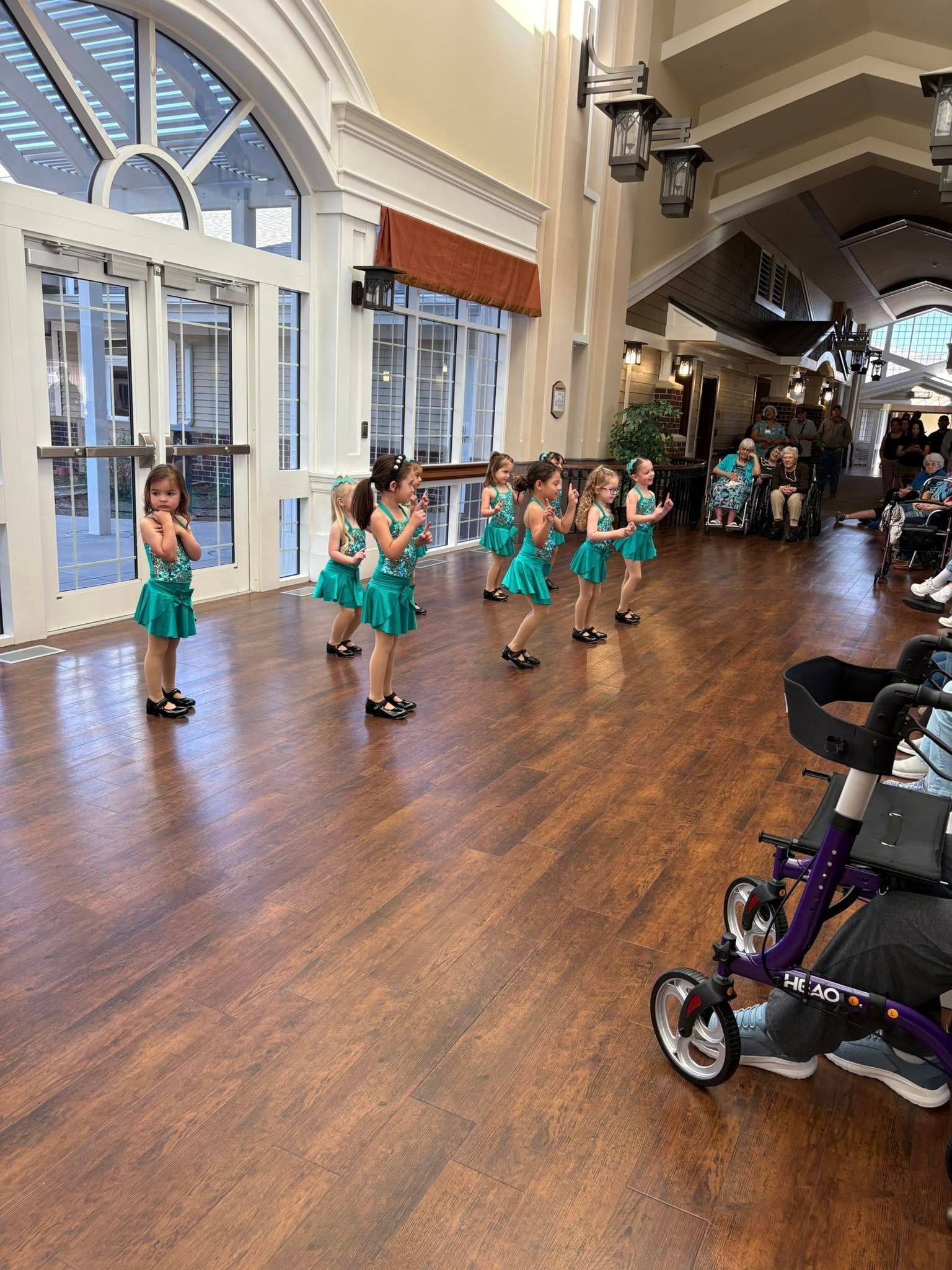 Young dancers in teal costumes perform indoors, possibly for an audience.