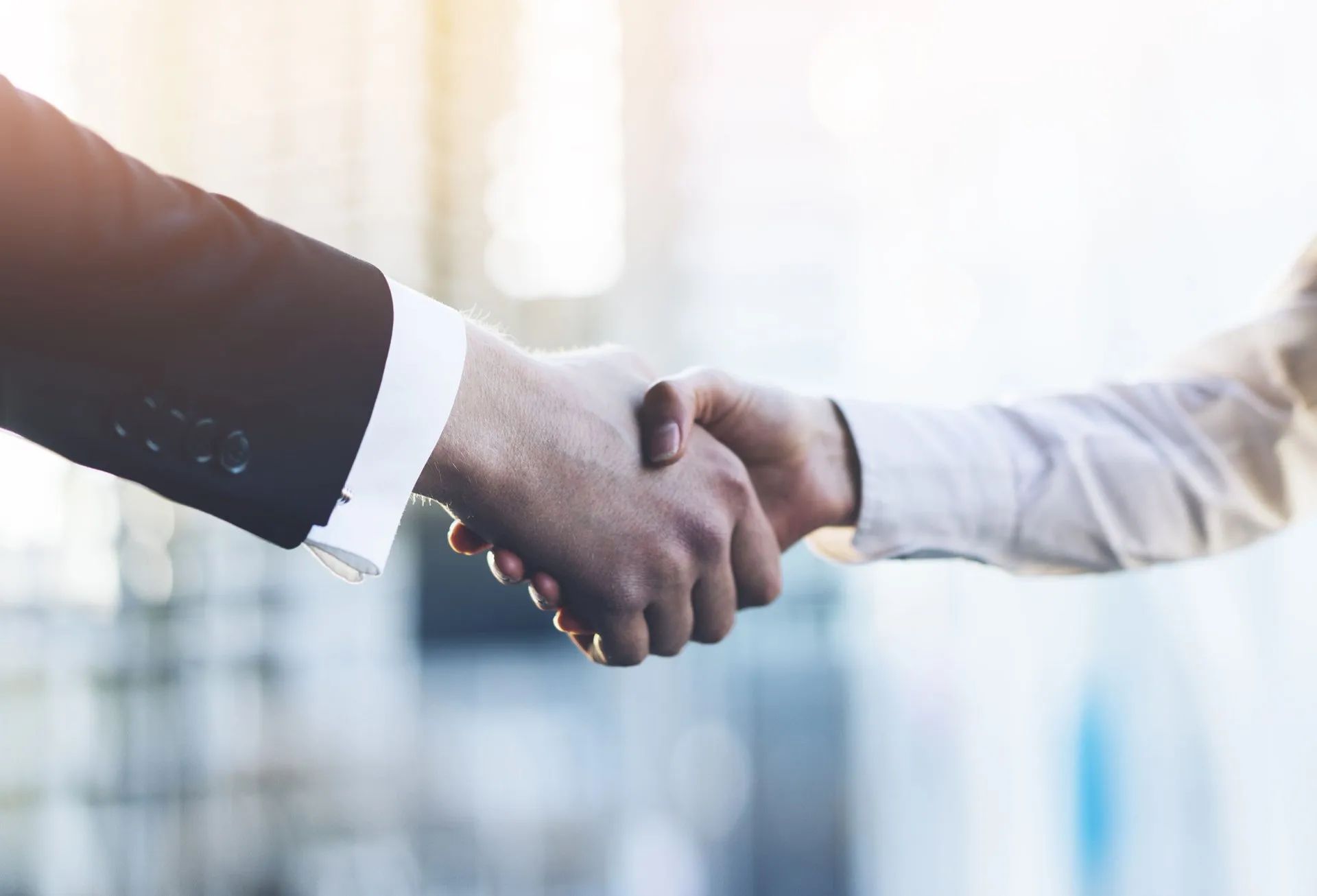 Two people in business attire shaking hands, blurred background.