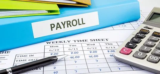 Payroll documents with a calculator and pen on a time sheet.