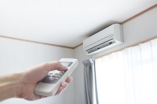 Hand holding remote, pointing toward a wall-mounted air conditioner in a room.