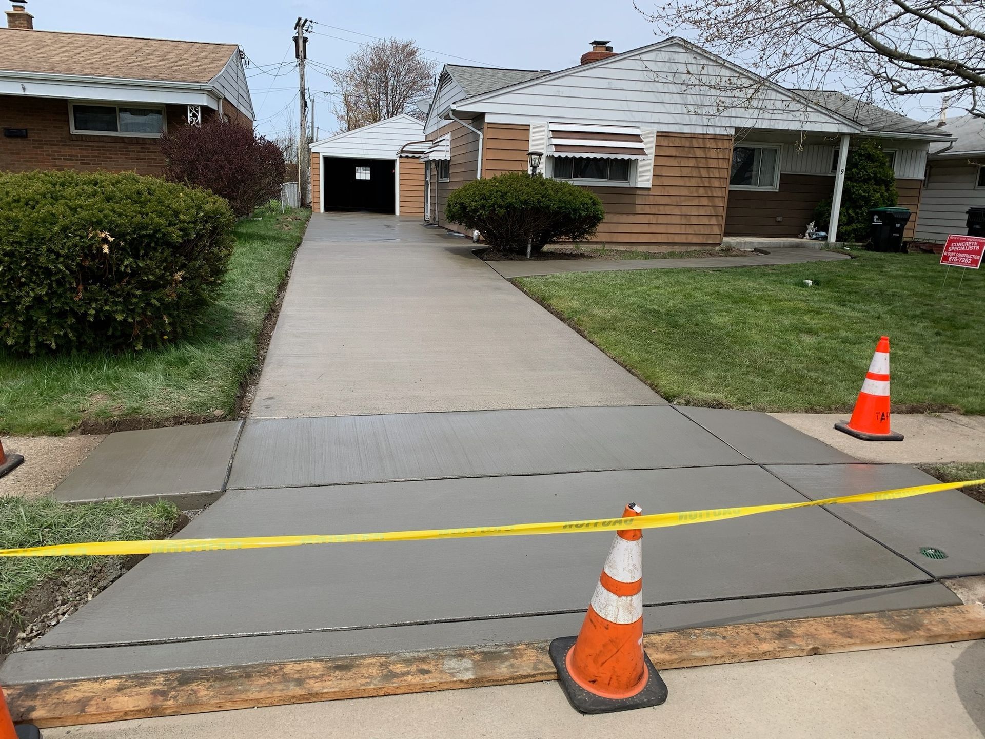 A concrete driveway leading to a house with orange and white traffic cones.