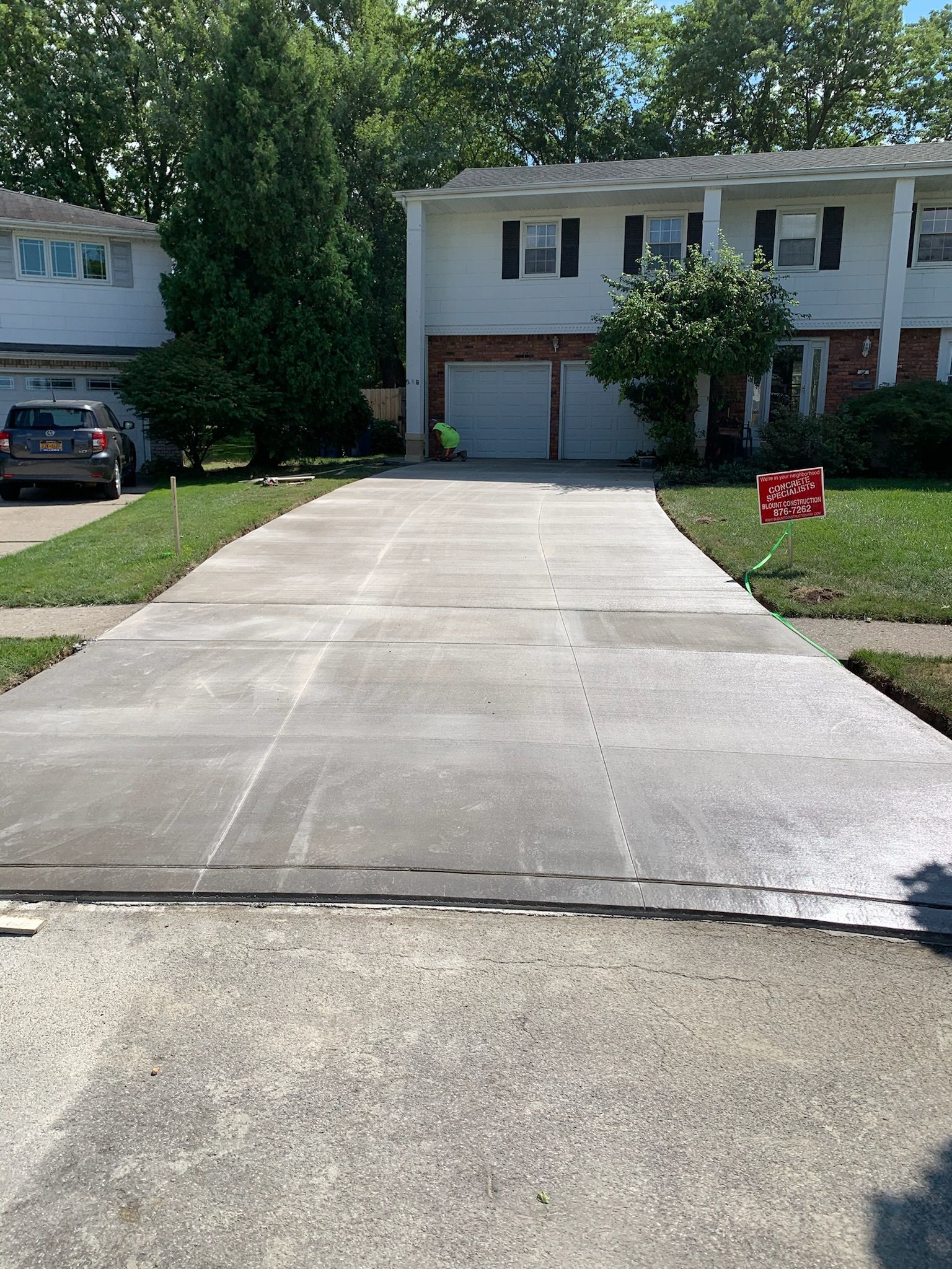 A concrete driveway leading to a house with a car parked in the driveway.