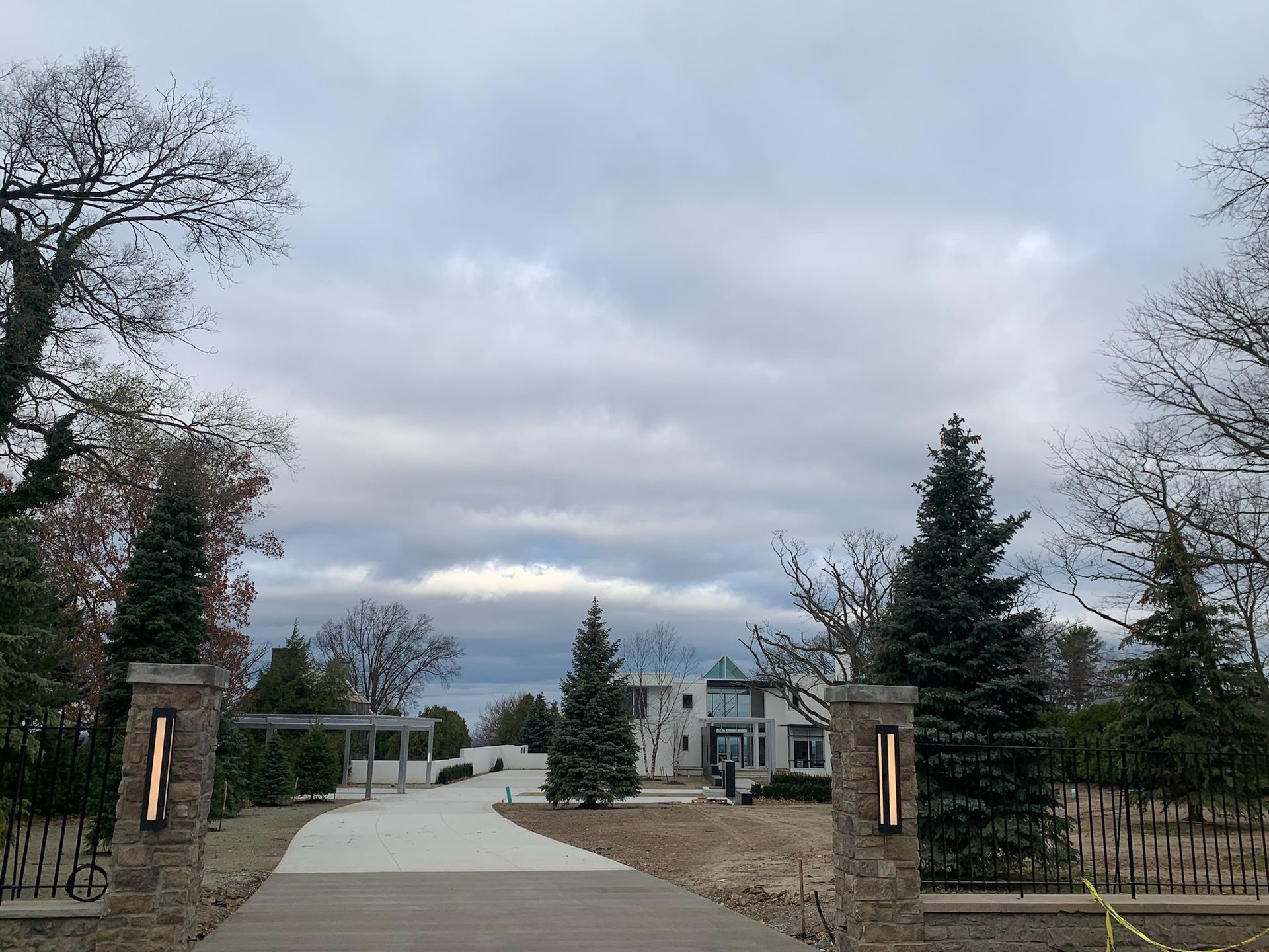 A driveway leading to a large house surrounded by trees on a cloudy day.