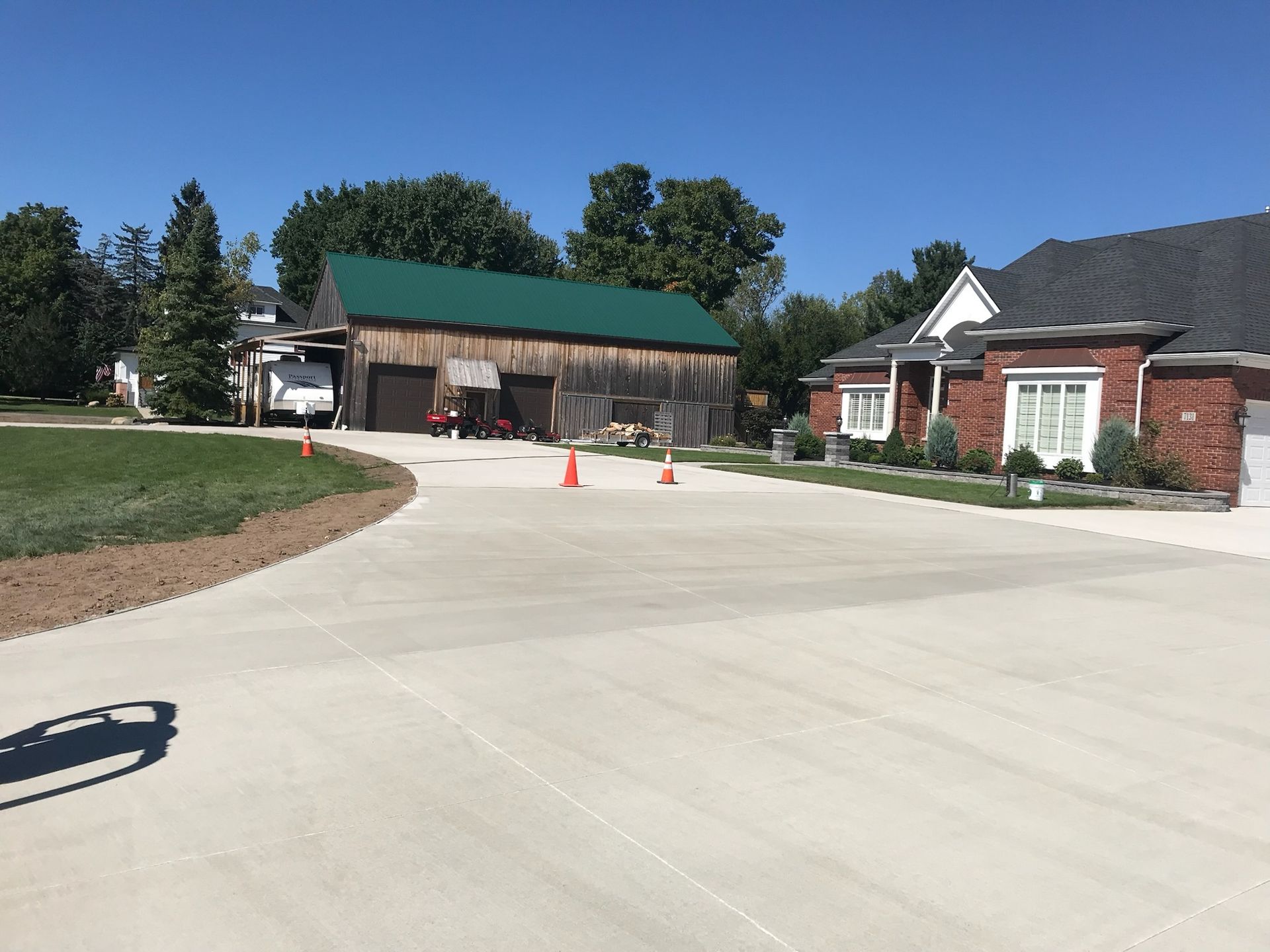 A concrete driveway leading to a brick house with a green barn in the background.