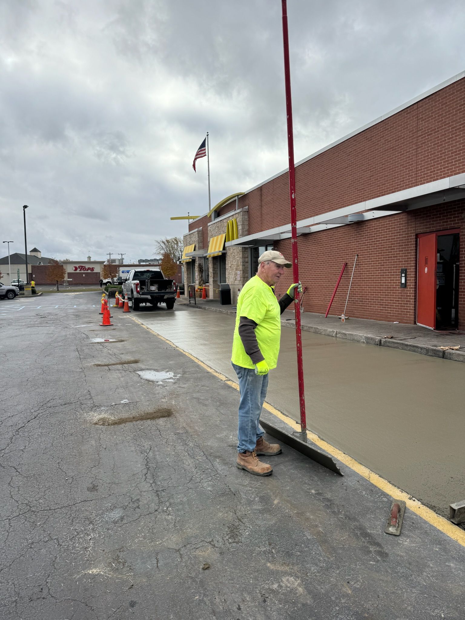 A man in a neon yellow shirt is sweeping the sidewalk in front of a building.