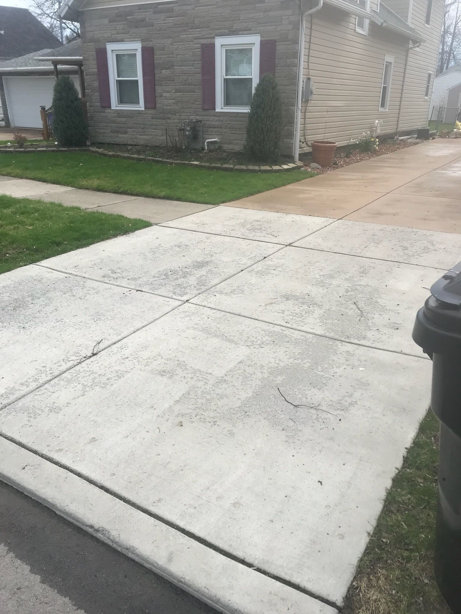 A concrete driveway with a trash can in front of a house.