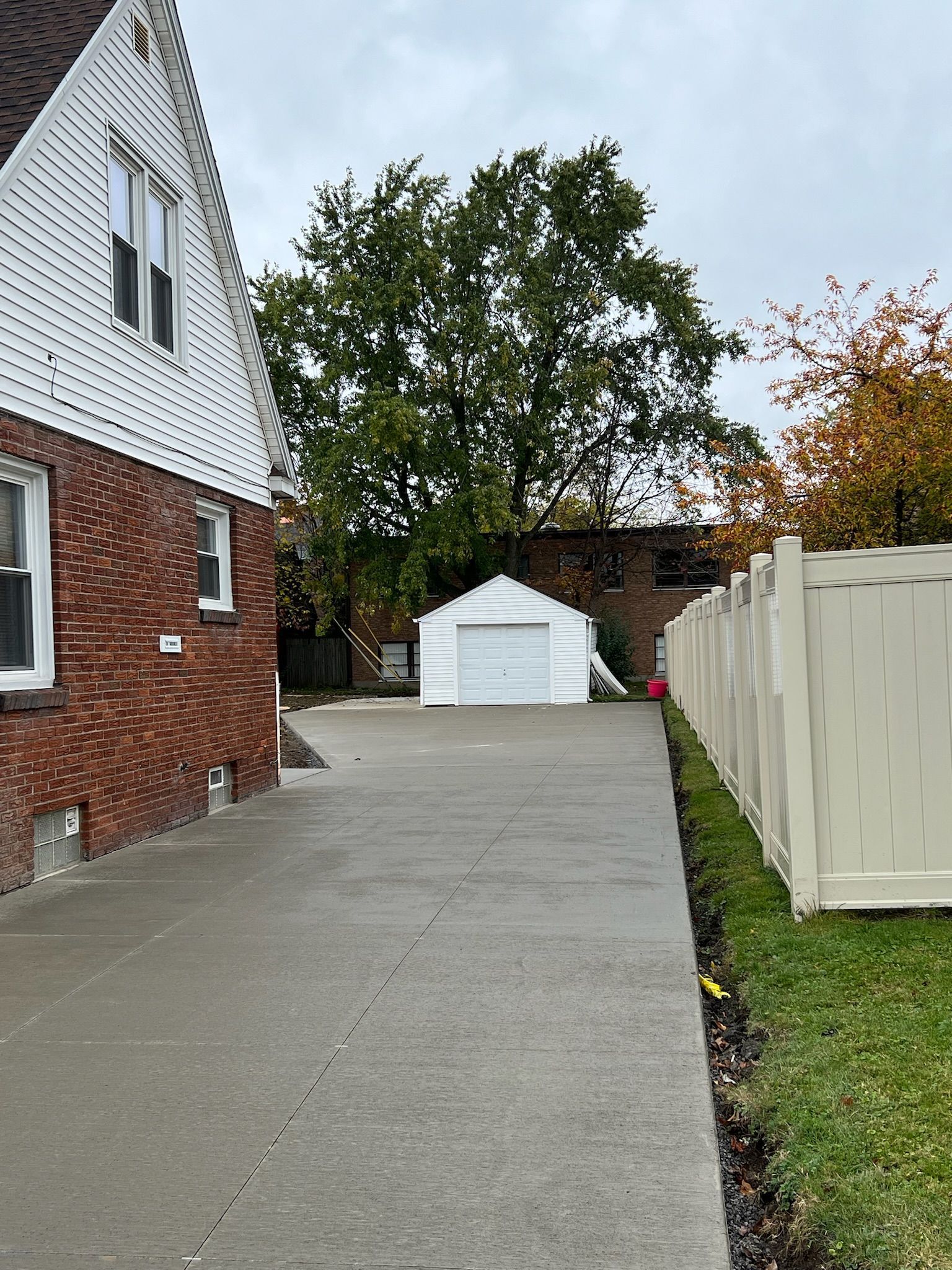 A driveway leading to a brick house with a white garage and a white fence.