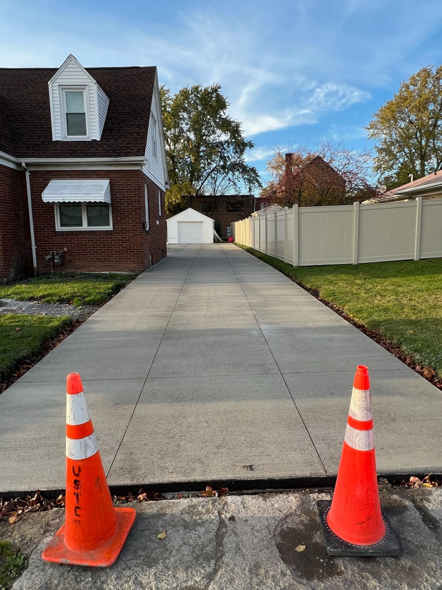 Two orange and white traffic cones are sitting on the side of a concrete driveway.