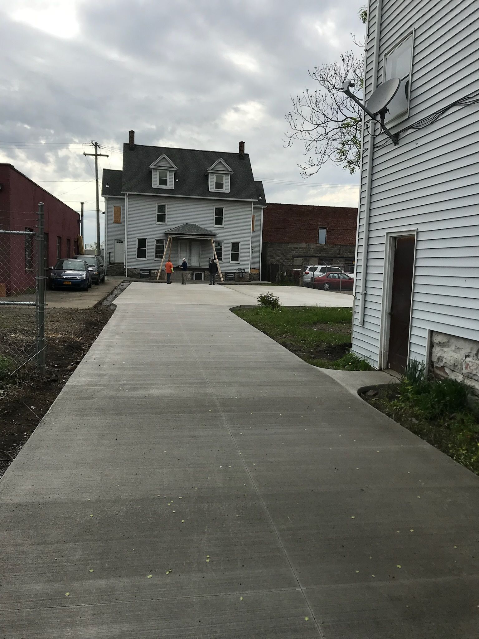 A concrete walkway leading to a house with a satellite dish on the side