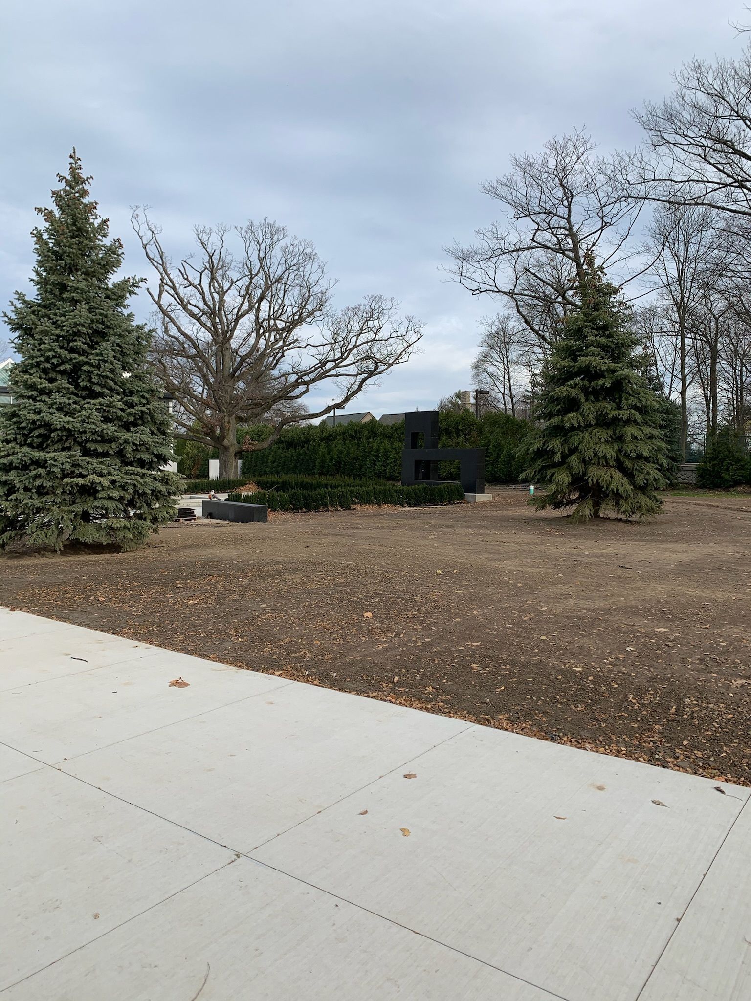 A concrete sidewalk leading to a dirt field with trees in the background