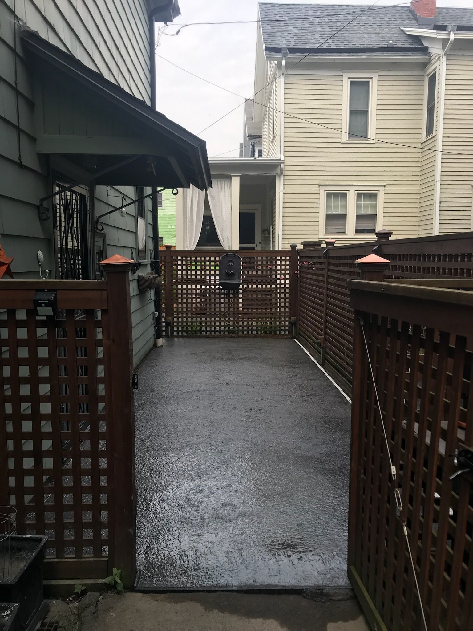 A wooden gate leads to a driveway between two houses.