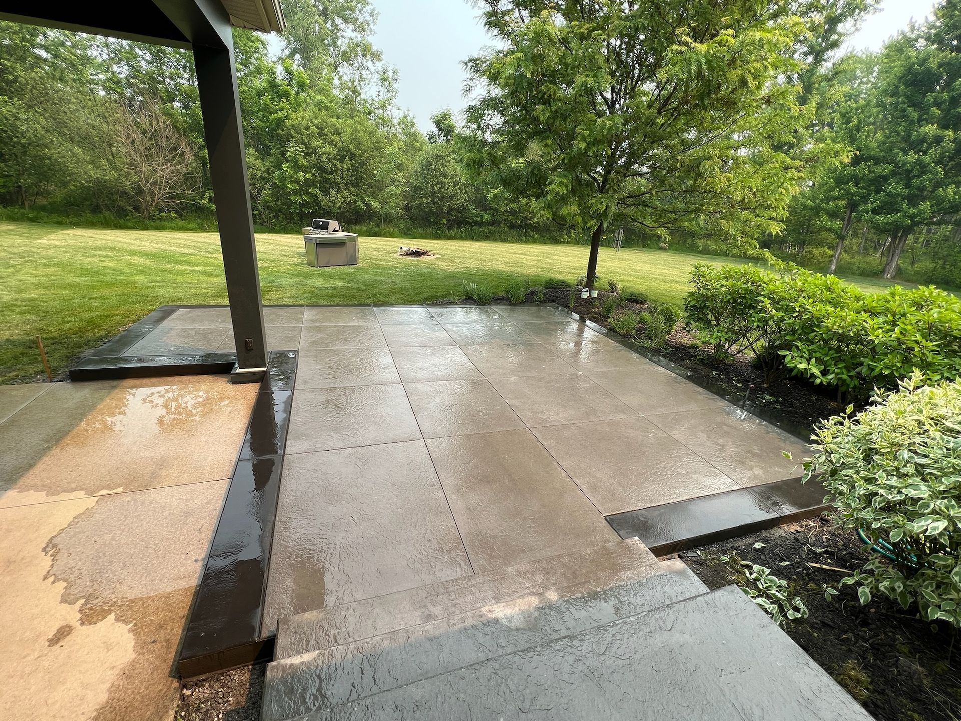 A patio in a backyard with a covered porch and trees in the background.