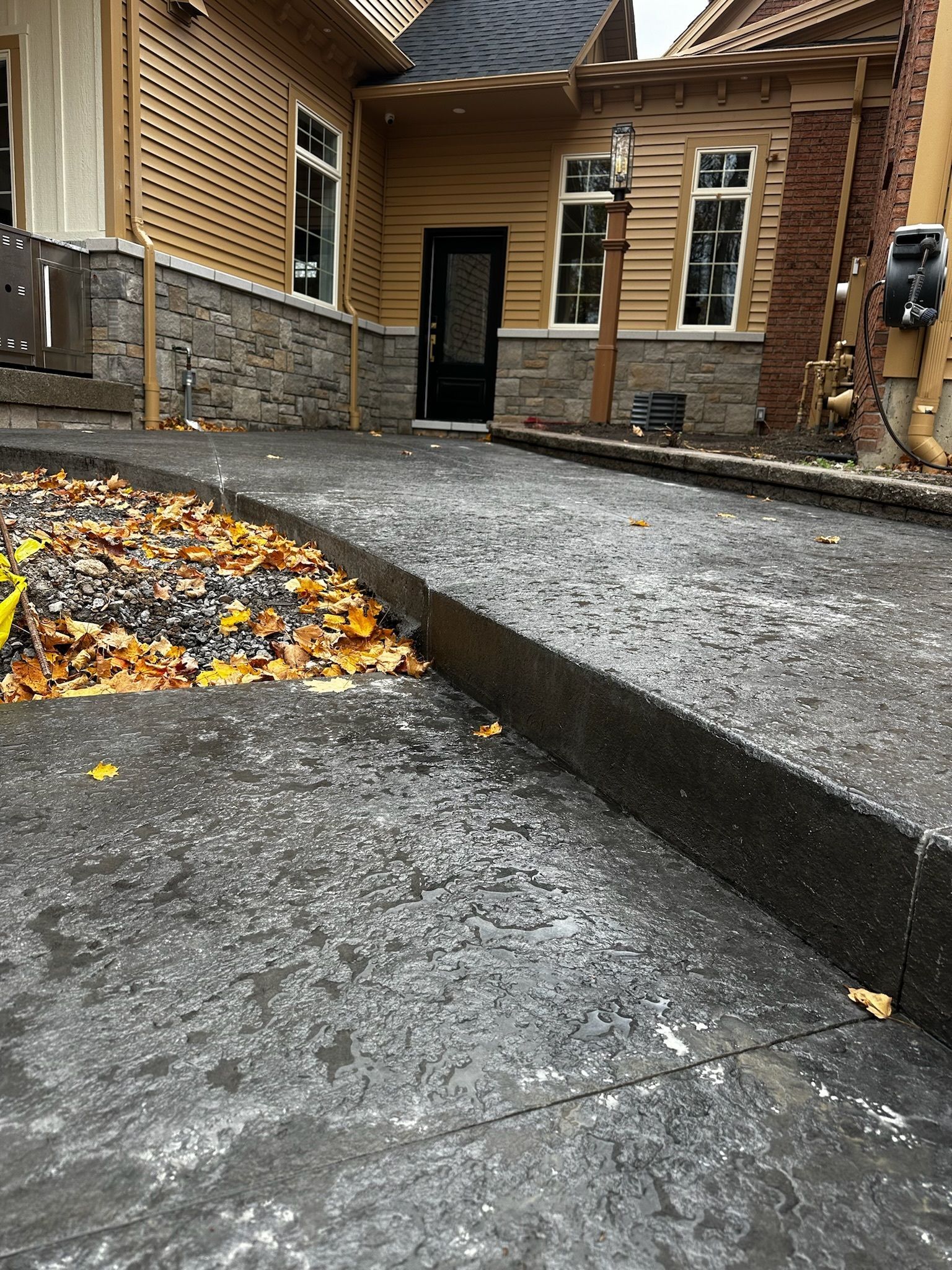 A concrete walkway leading to a house with leaves on the ground.