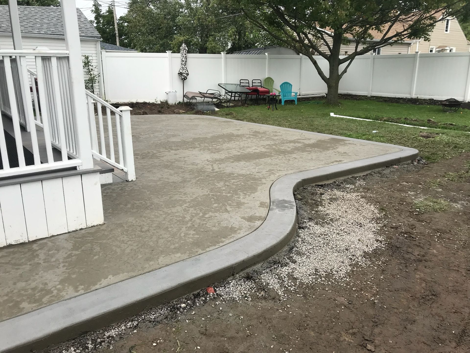 A concrete patio with a white railing and a tree in the background.