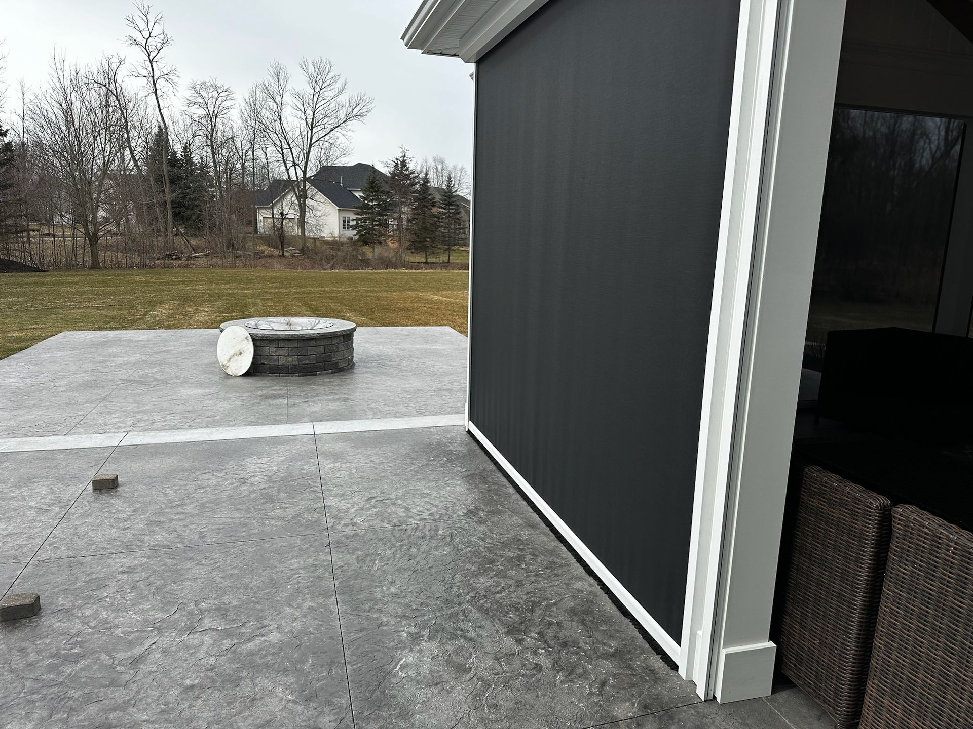 A patio with a fire pit and a black screen on the side of a house.