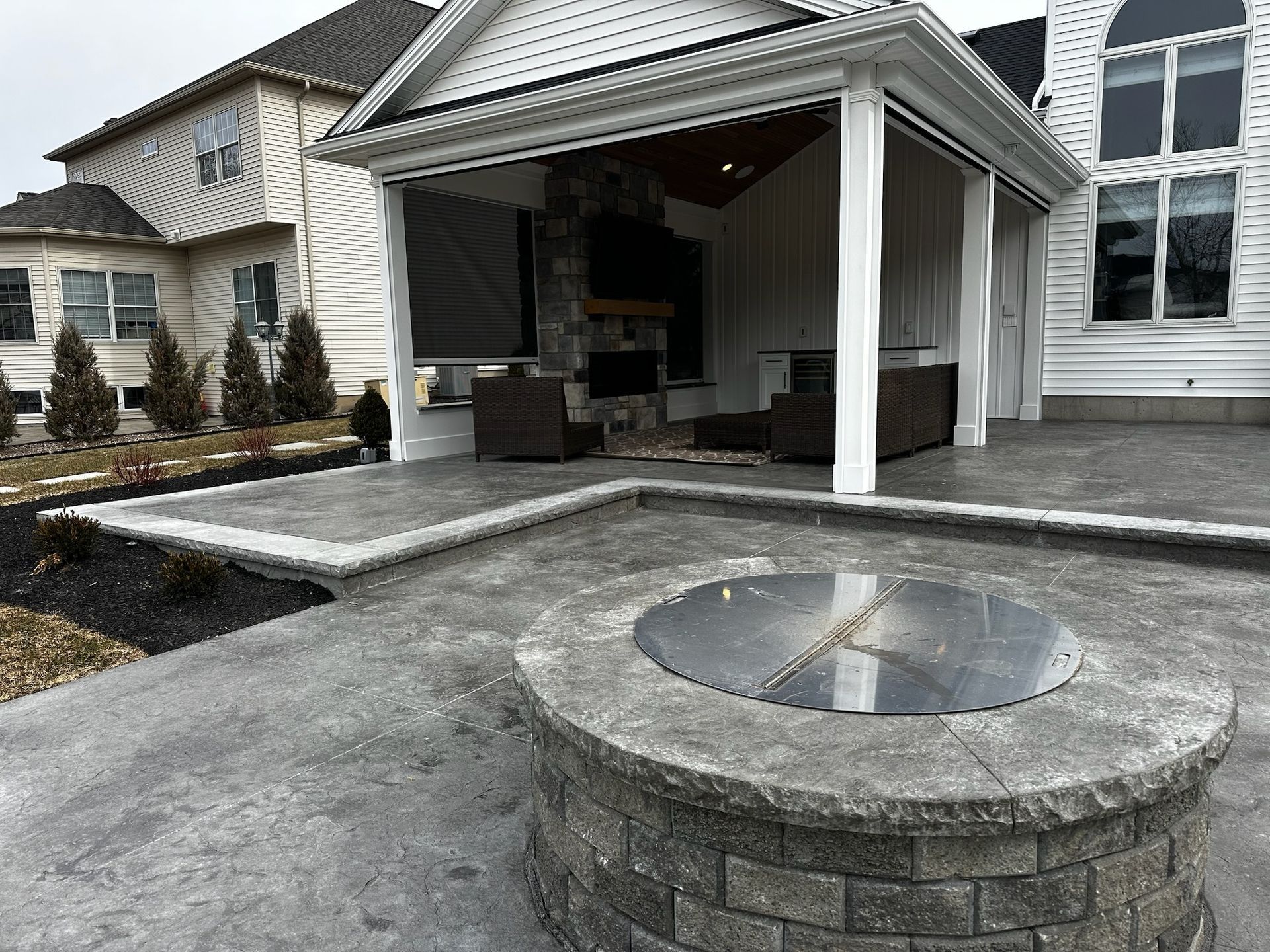 A fire pit is in the middle of a patio in front of a house.