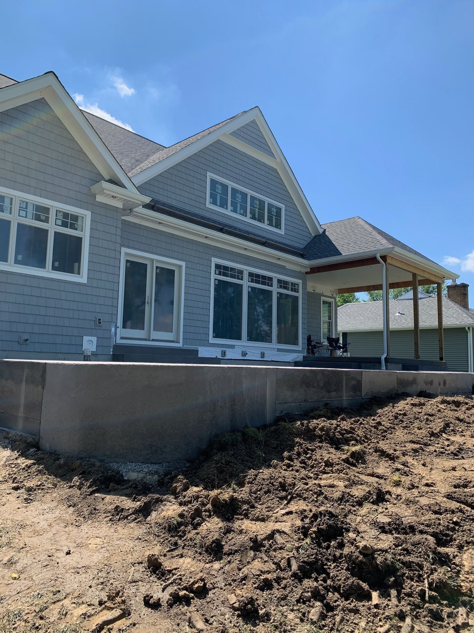 A large house with a porch is sitting on top of a dirt field.