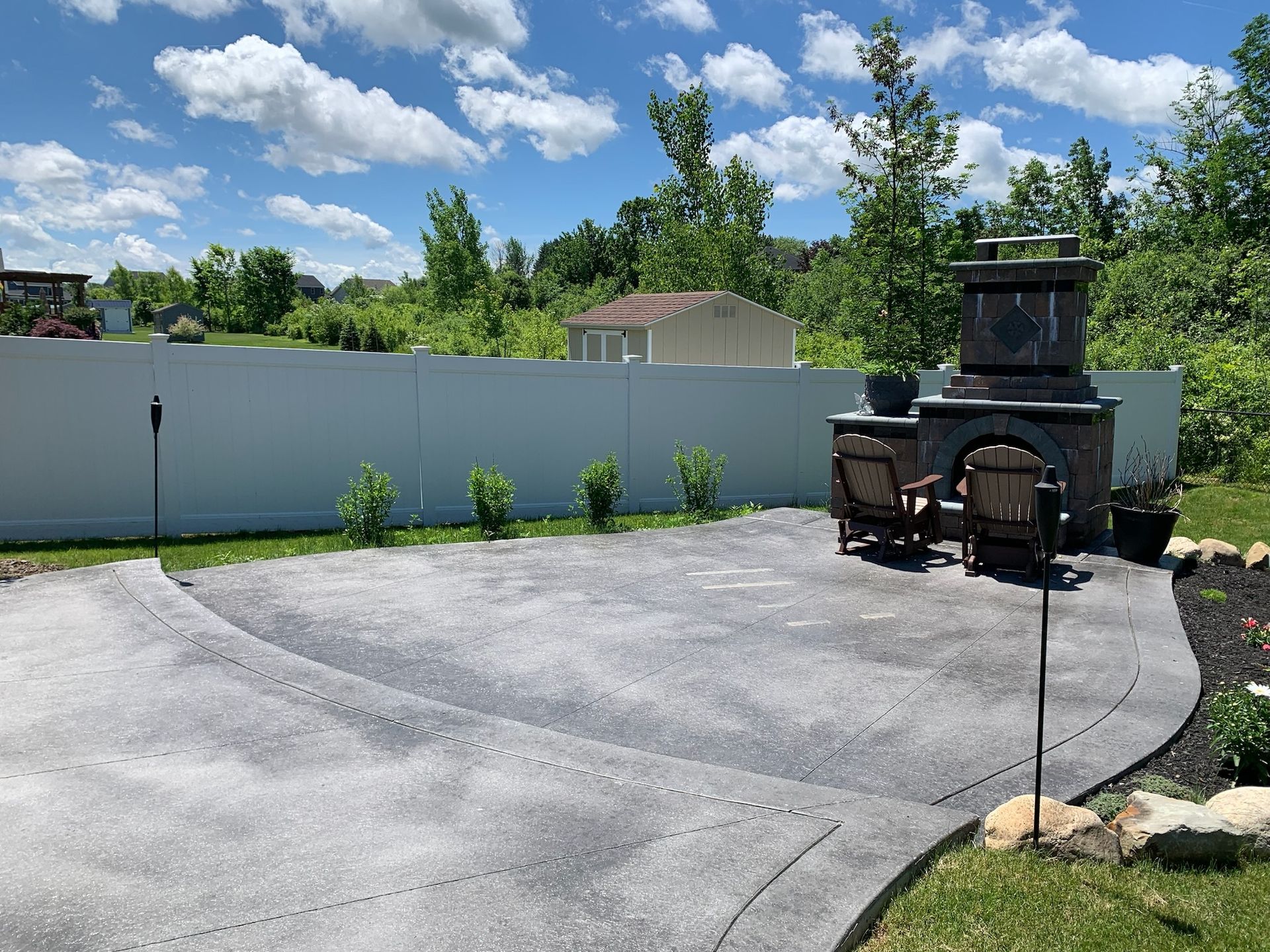 A patio with a fireplace and chairs in front of a white fence.