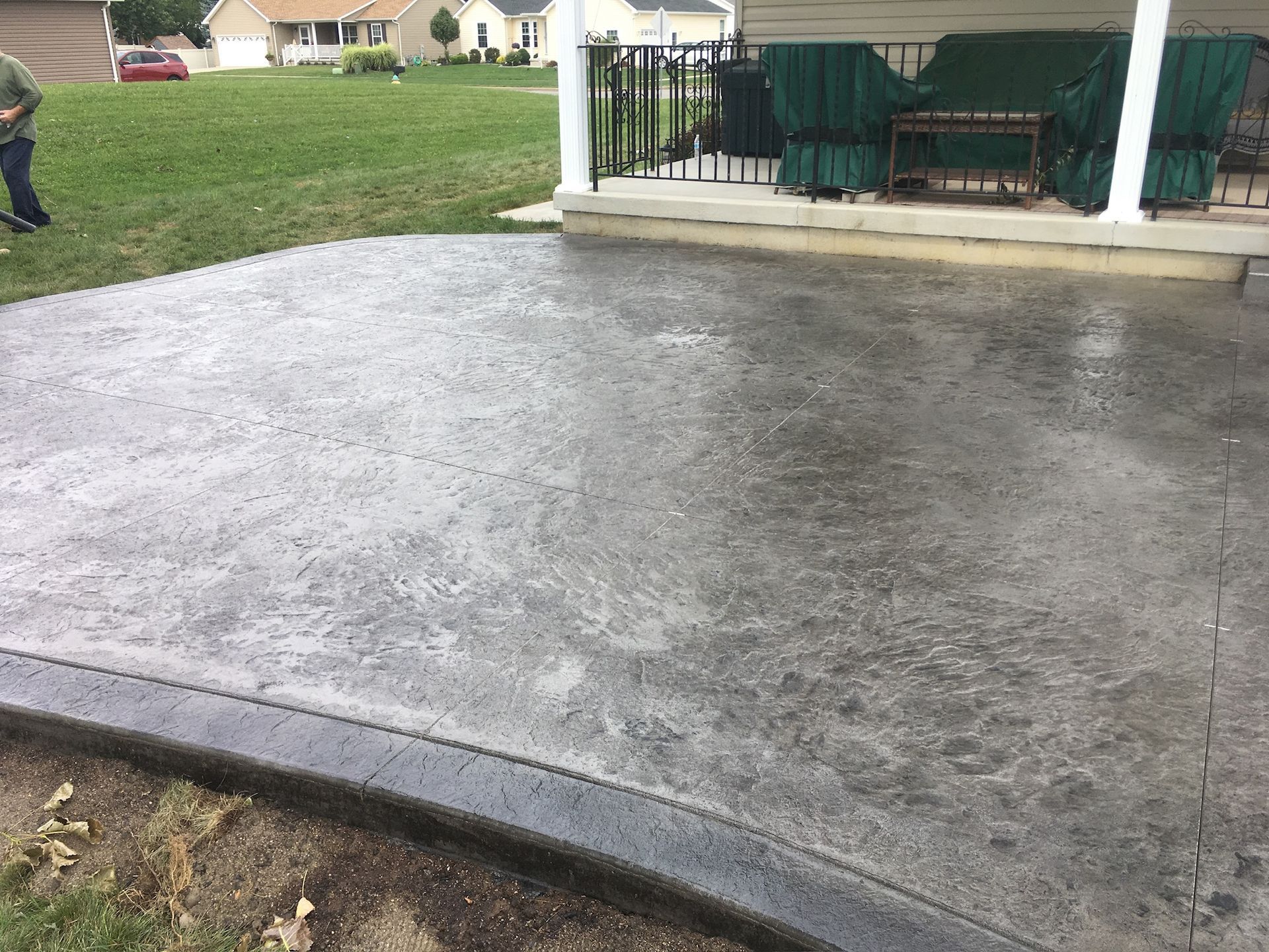 A man is standing on a concrete driveway next to a porch.