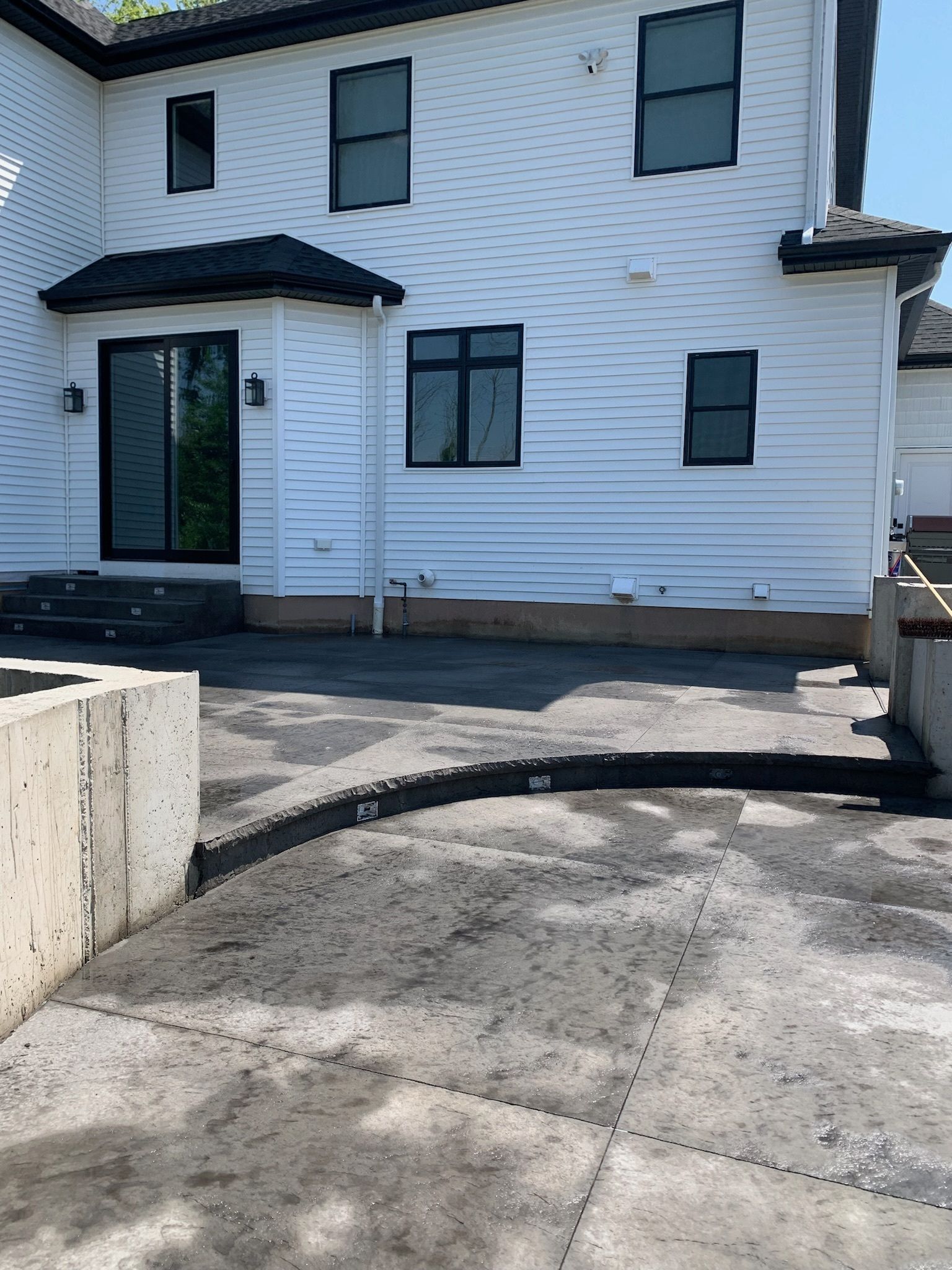 A white house with black windows and a concrete driveway in front of it.