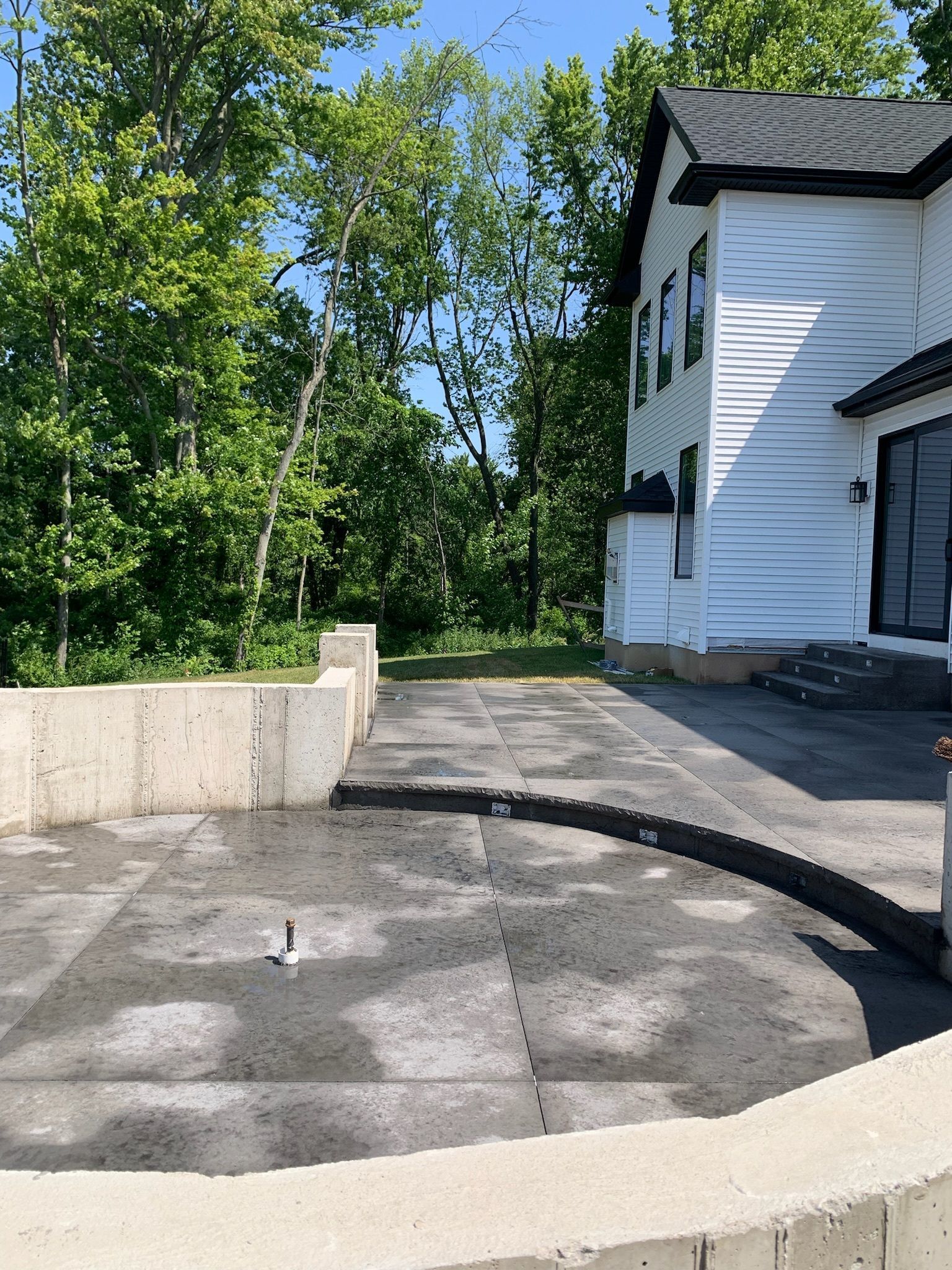A white house with a black roof is surrounded by trees and a concrete driveway.