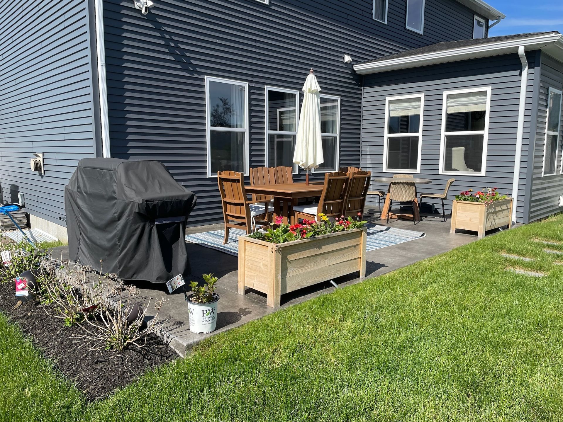 A patio with a table and chairs and a grill in front of a house.