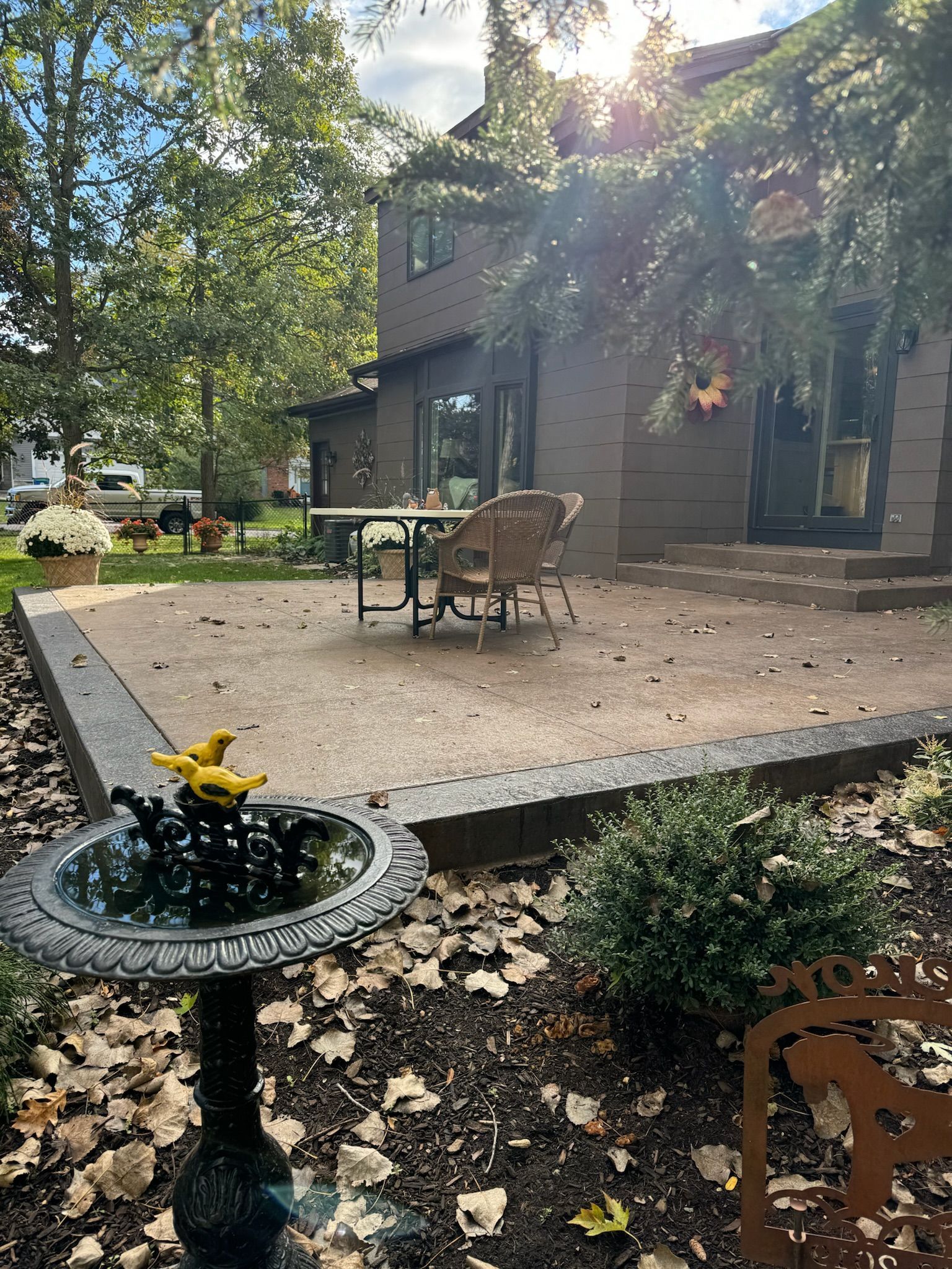 A bird bath is in the middle of a patio in front of a house.