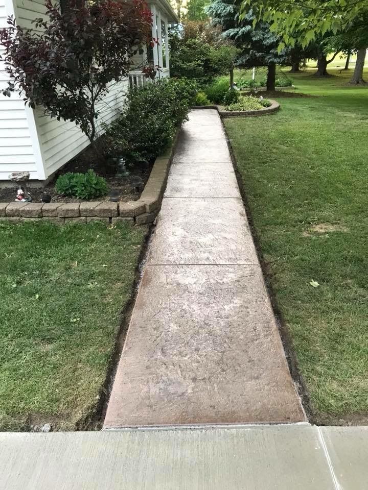 A concrete walkway leading to a house with a lush green lawn.