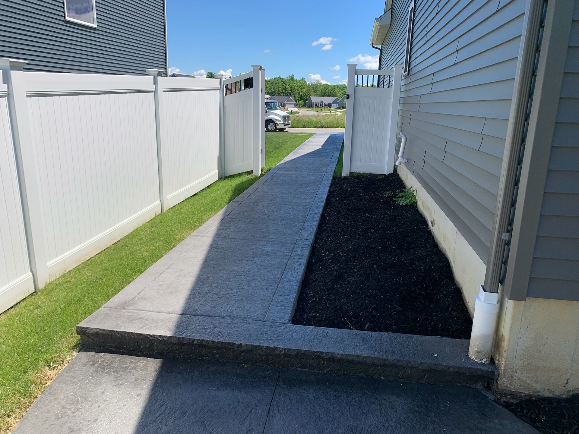 A sidewalk leading to a house with a white fence.