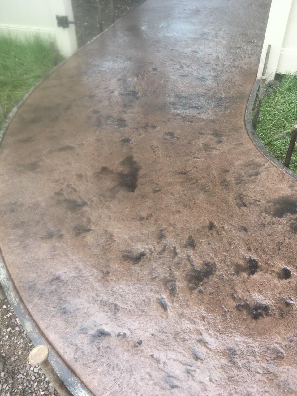 A concrete walkway leading to a house with a fence in the background.