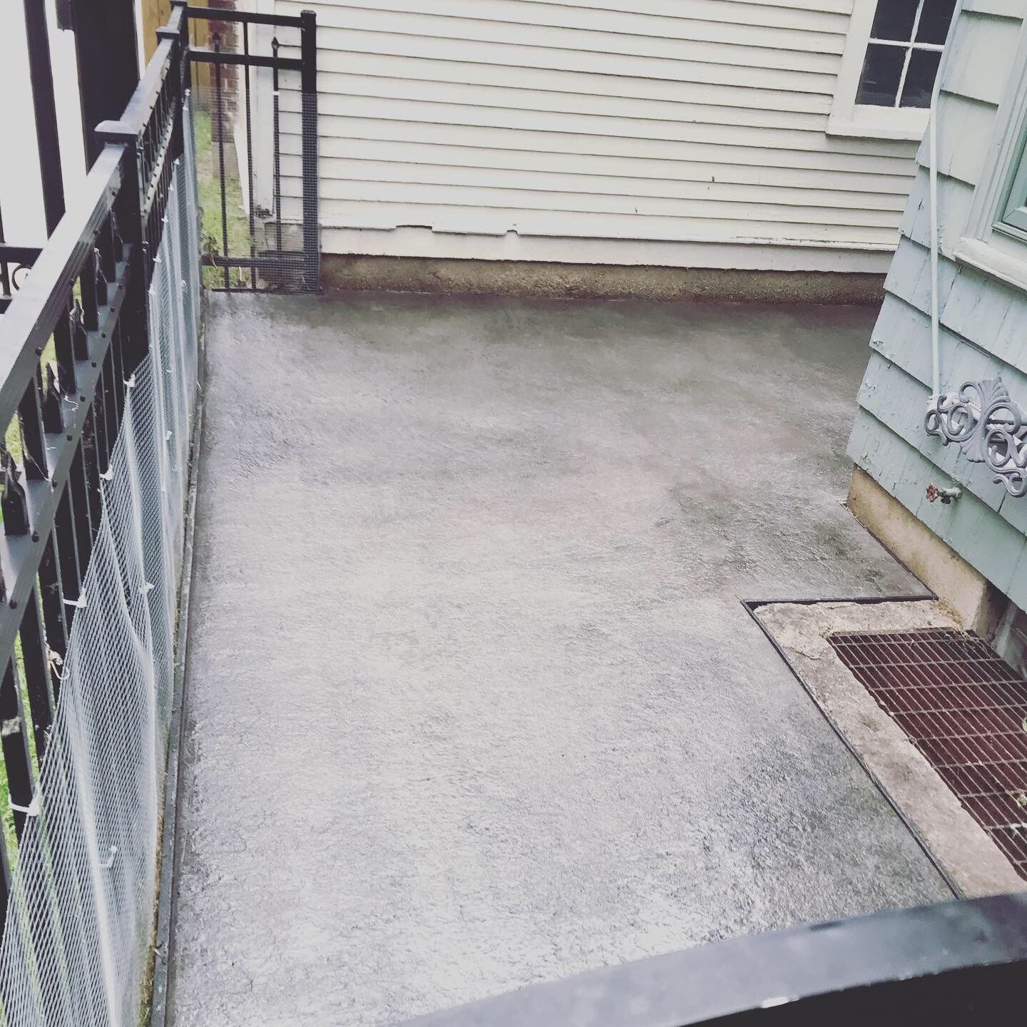 A concrete walkway leading to a house with a chain link fence