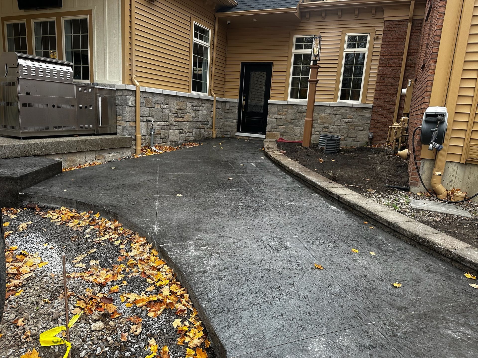 A driveway leading to a house with a grill in the background.