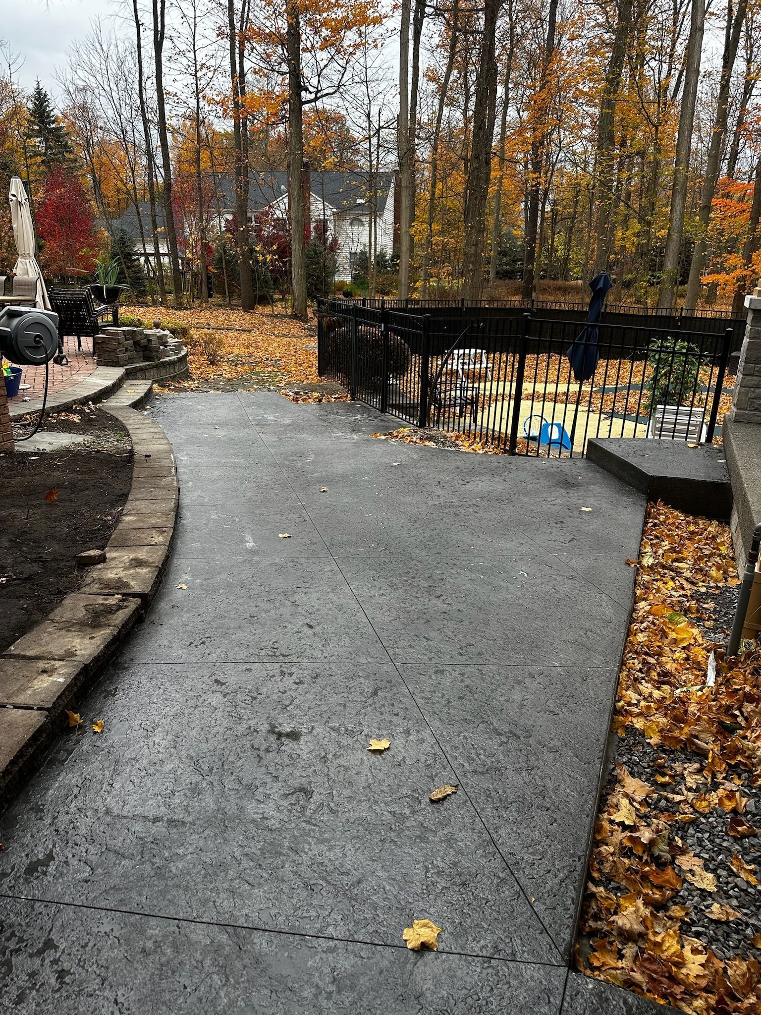 A concrete driveway surrounded by trees and leaves on a rainy day.