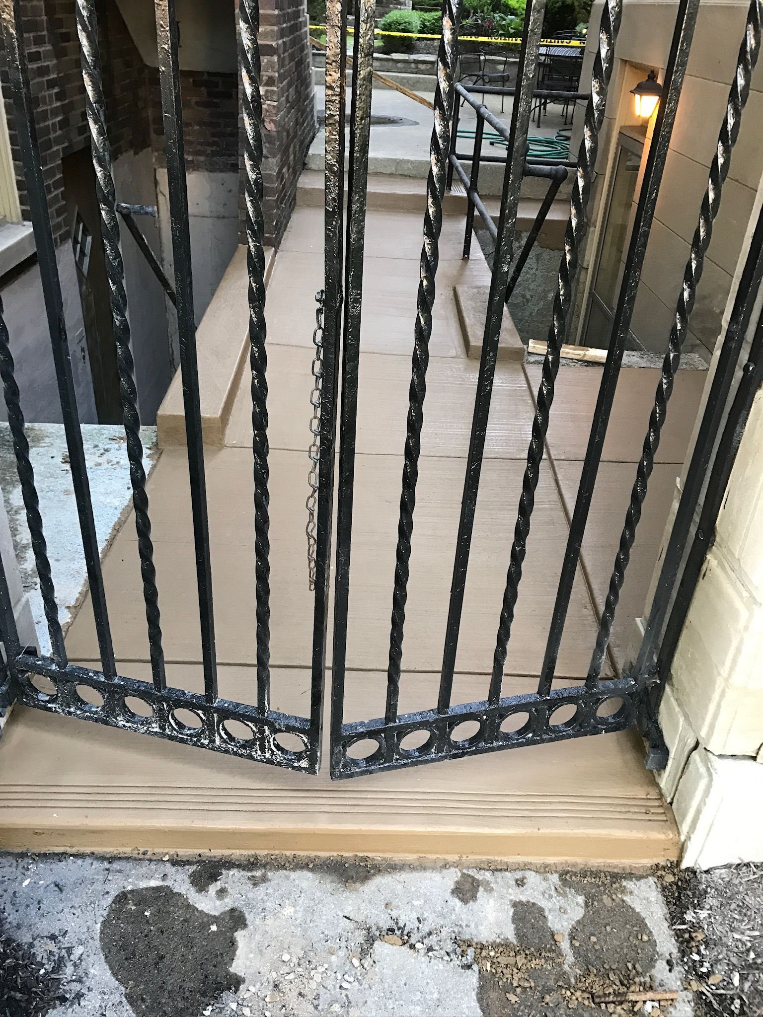A wrought iron gate is open to a tiled walkway.