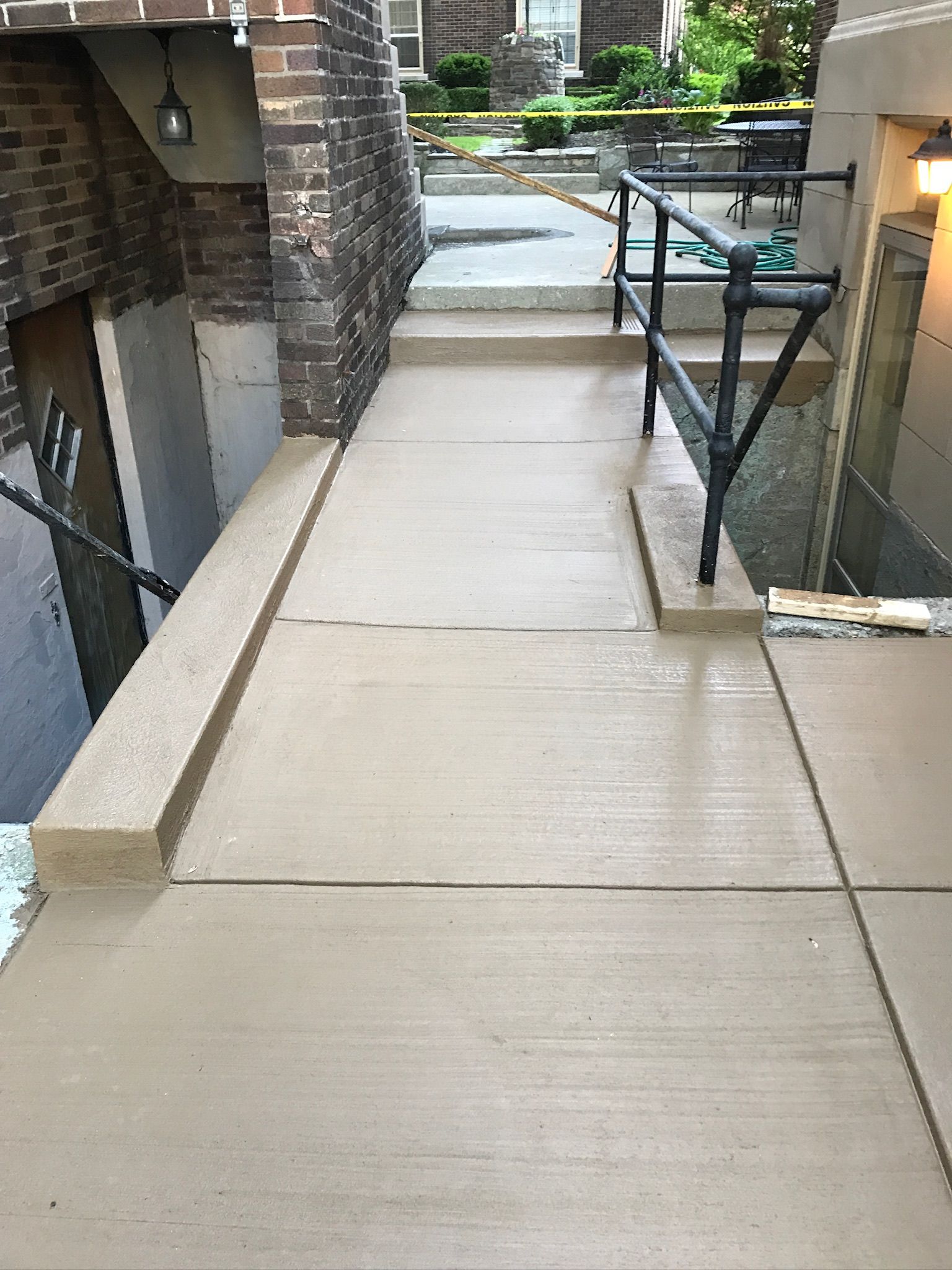 A concrete walkway leading to a basement with stairs and a railing.