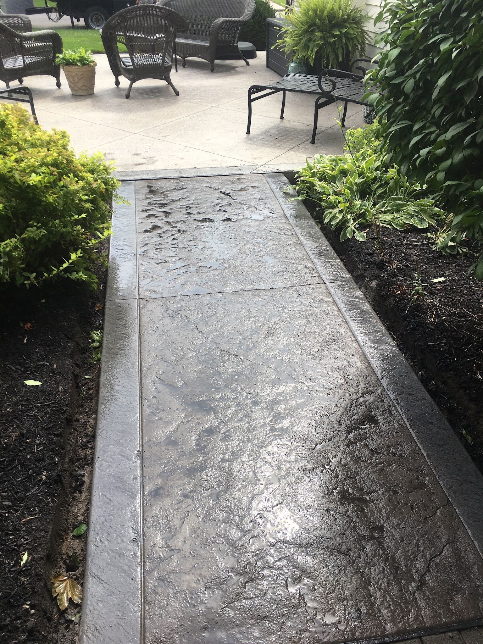 A concrete walkway leading to a patio with chairs and tables.