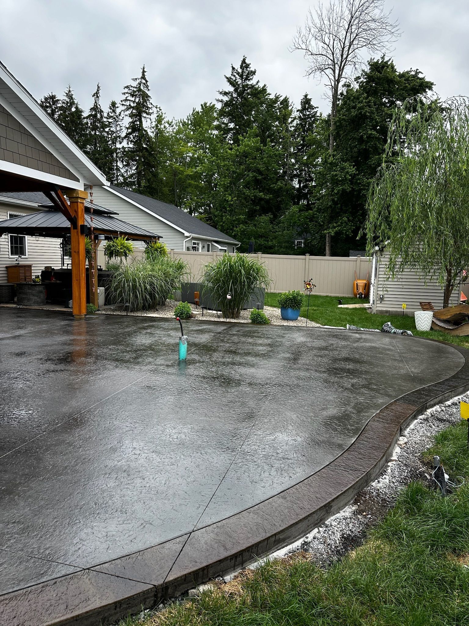 A concrete driveway in front of a house on a rainy day.
