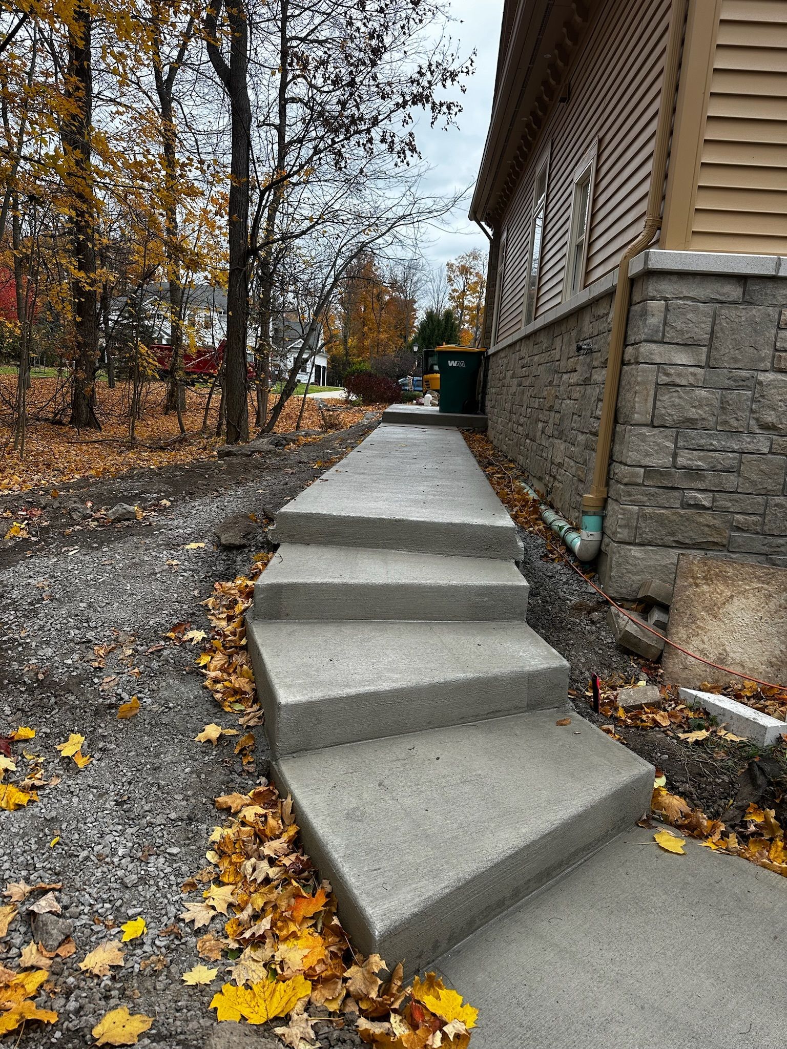 A concrete walkway leading to a house with leaves on the ground.