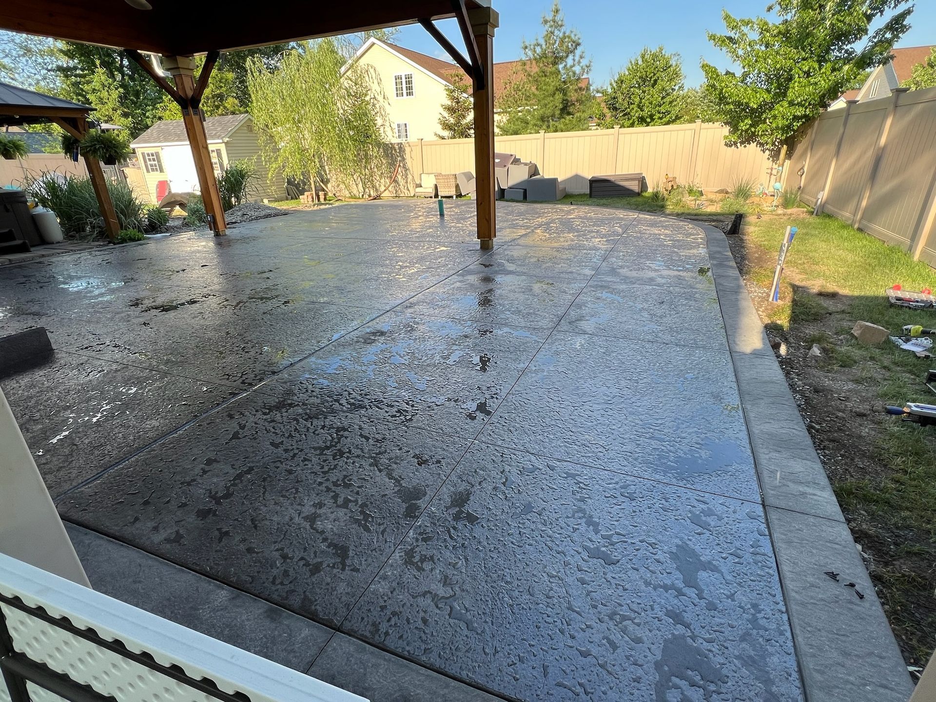 A concrete patio with a gazebo and a fence in the background.