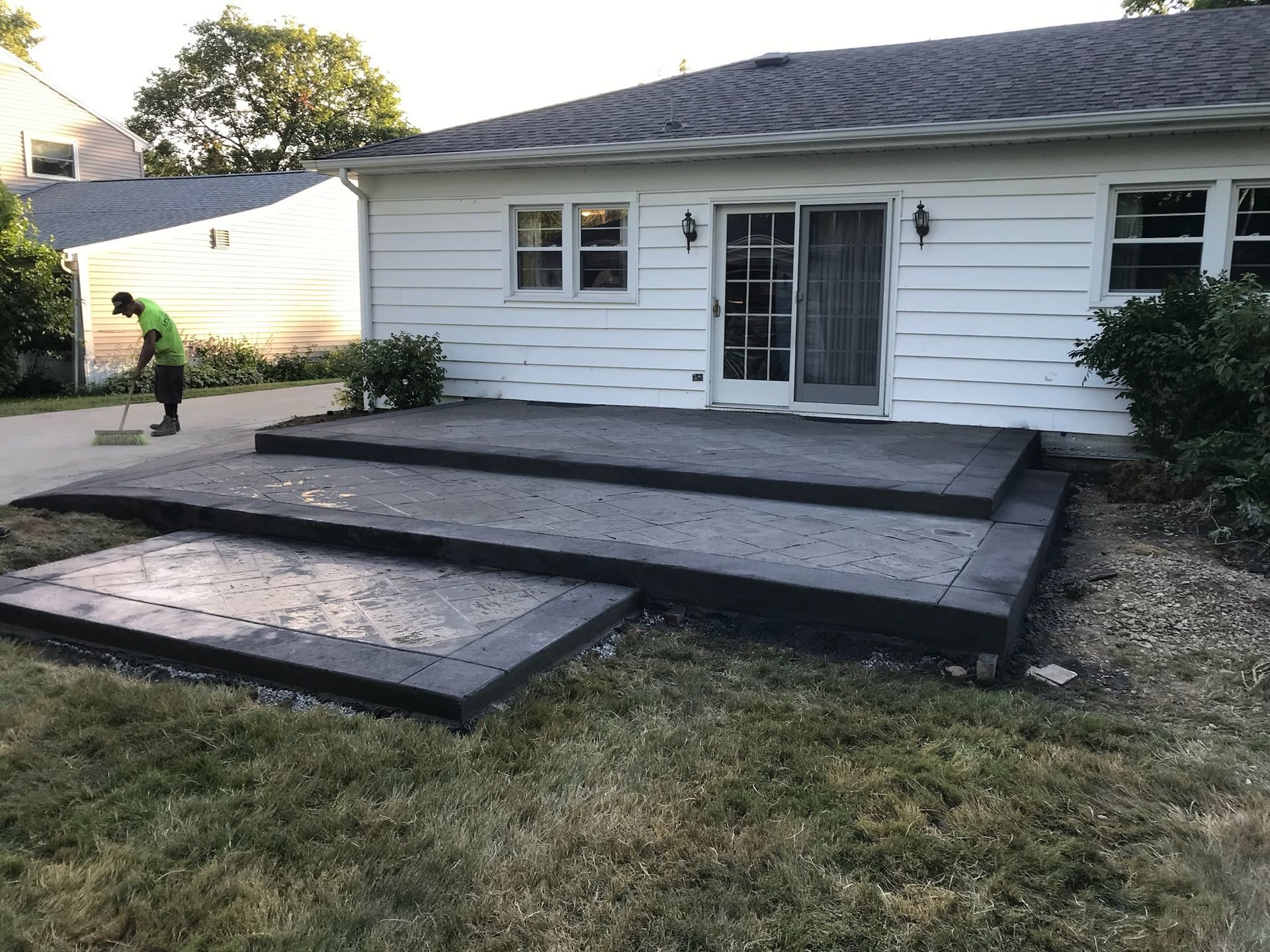 A man is sweeping the grass in front of a white house.