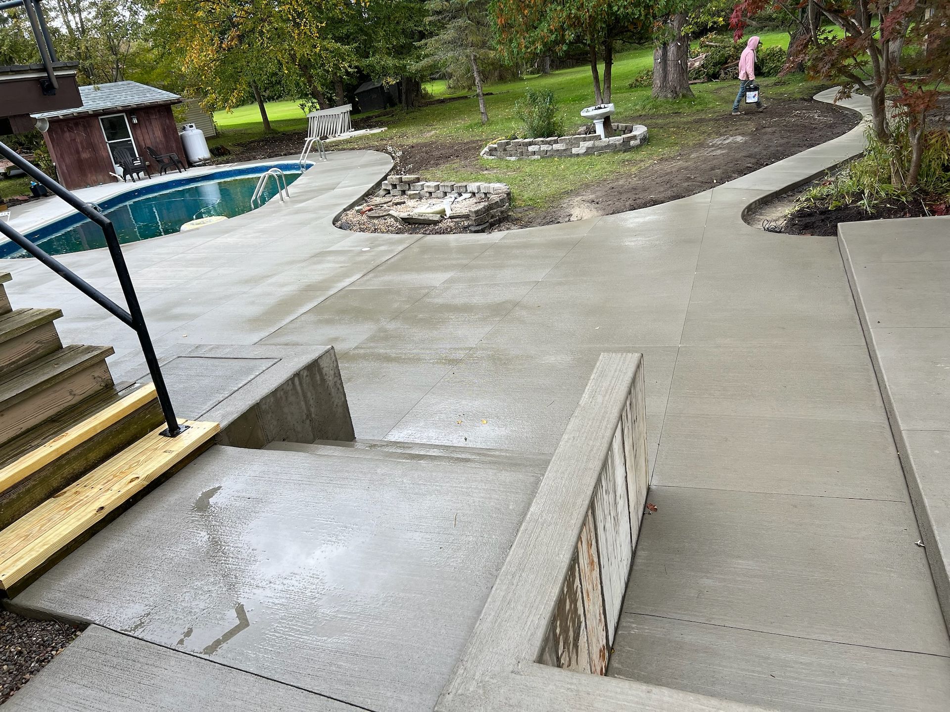 A concrete walkway leading to a pool in a backyard.