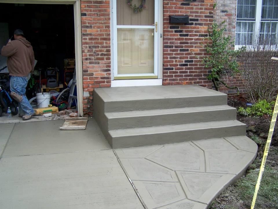 A man is standing in front of a brick house with concrete steps