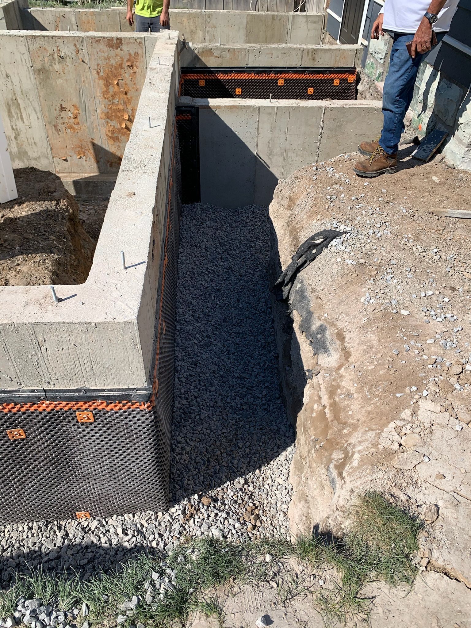A man is standing on top of a pile of gravel next to a concrete wall.
