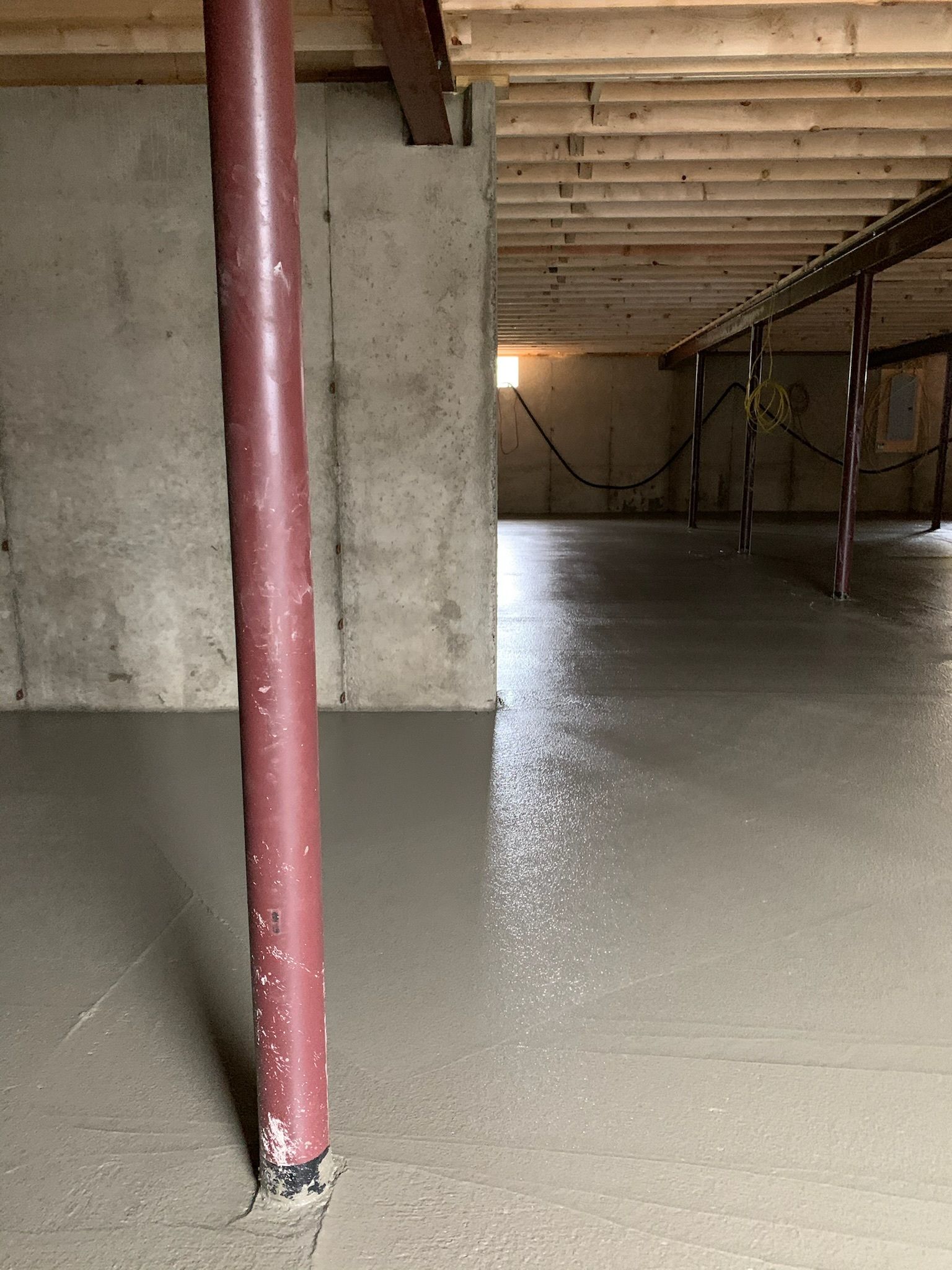 A concrete floor in a basement with a red pole in the middle.