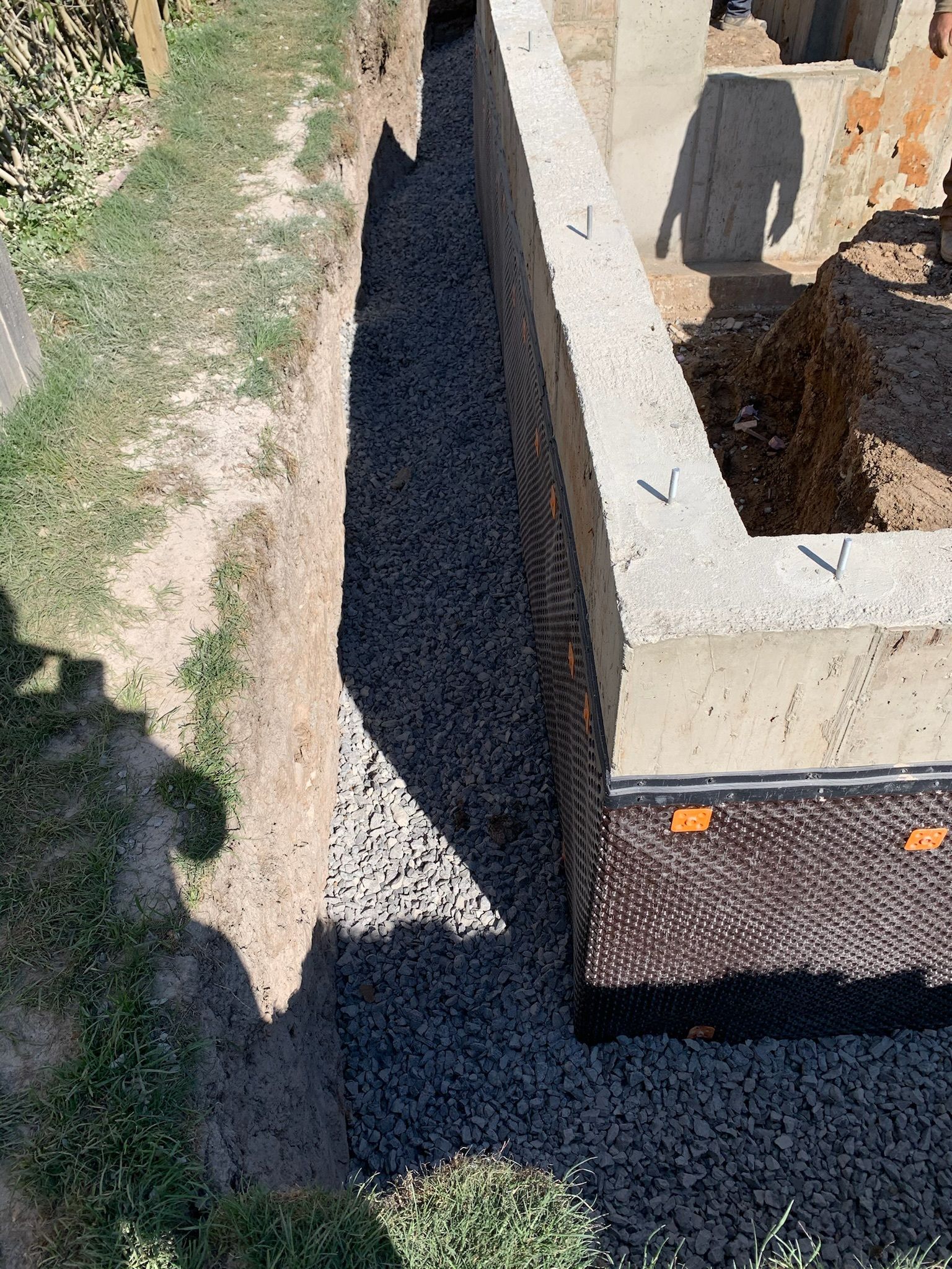A person is digging a hole in the ground next to a concrete wall.