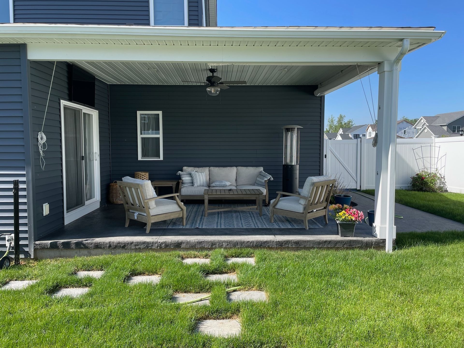 A covered patio with a couch , chairs , and a table in the backyard of a house.