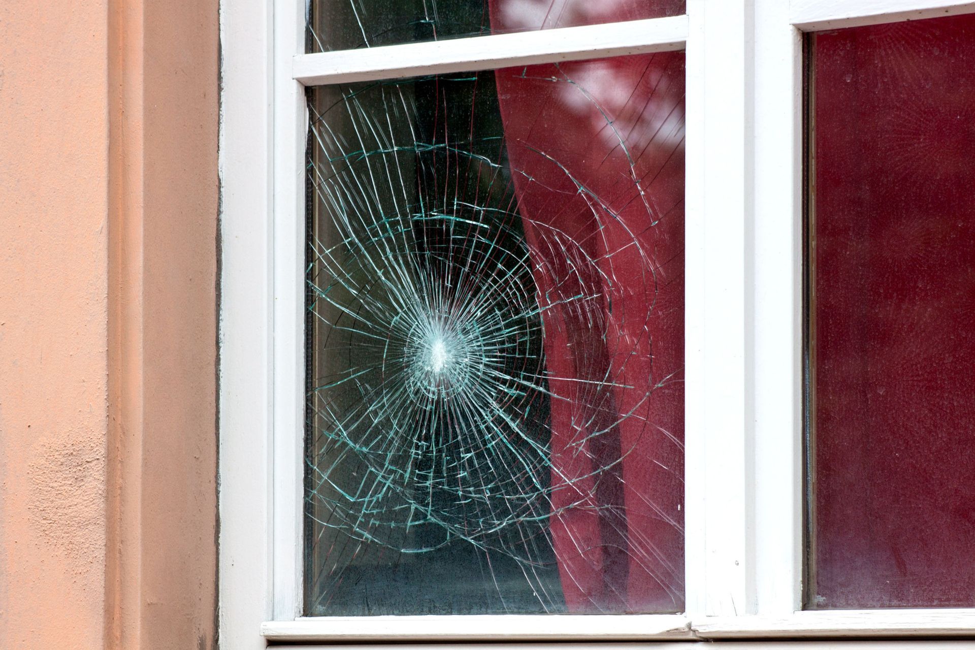Broken window, white frame, damage from impact with cracks radiating outward. Red curtain visible.