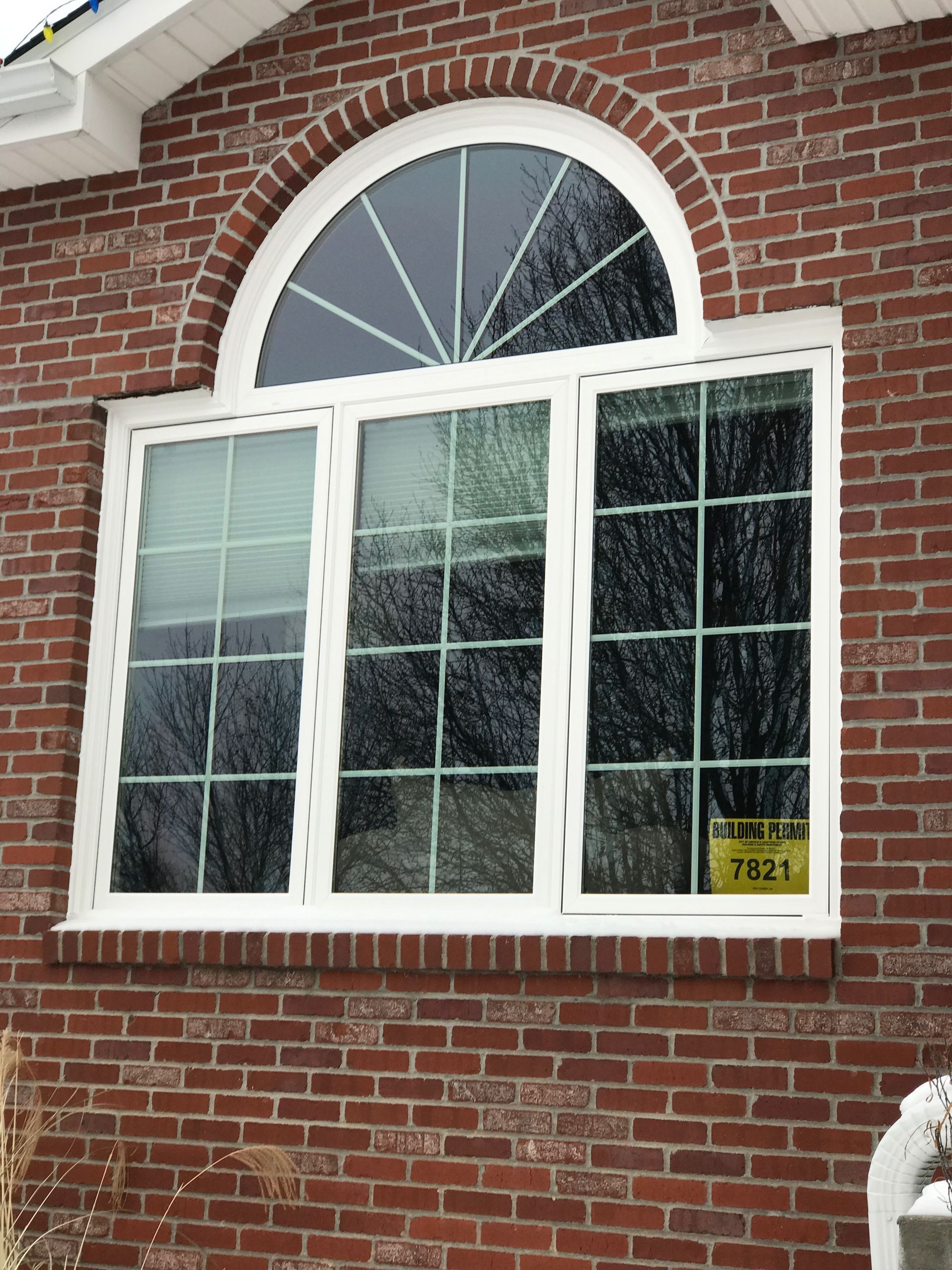 Brick building with arched window featuring a fanlight above three rectangular panes, white frames.