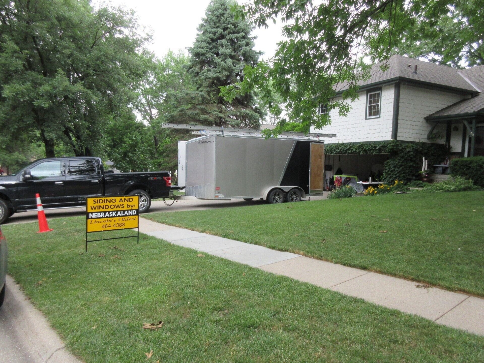 Black truck with trailer parked on residential lawn; sign on ground.